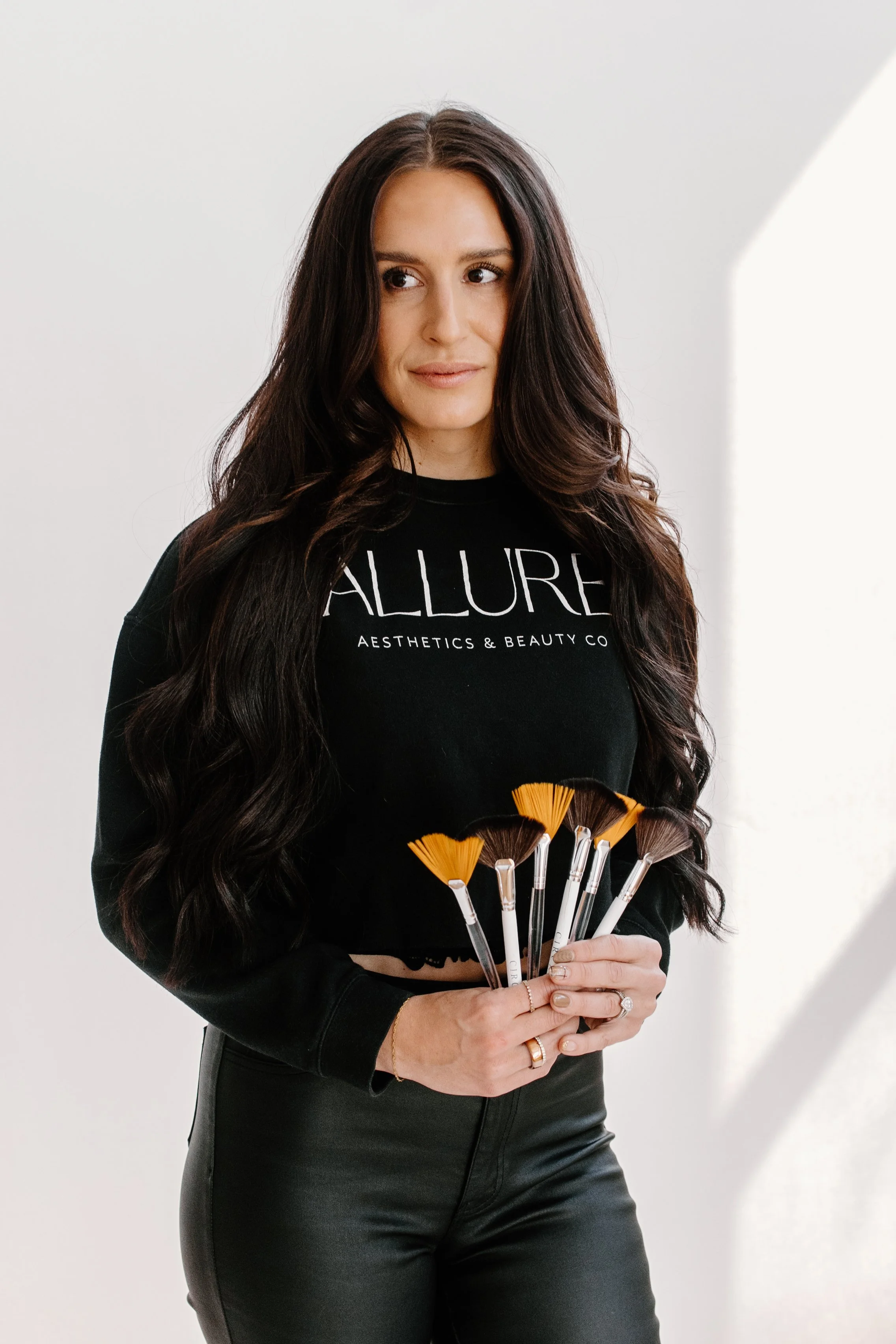 A woman with long brown hair holding a small blue bottles towards the camera, focusing on the bottle.