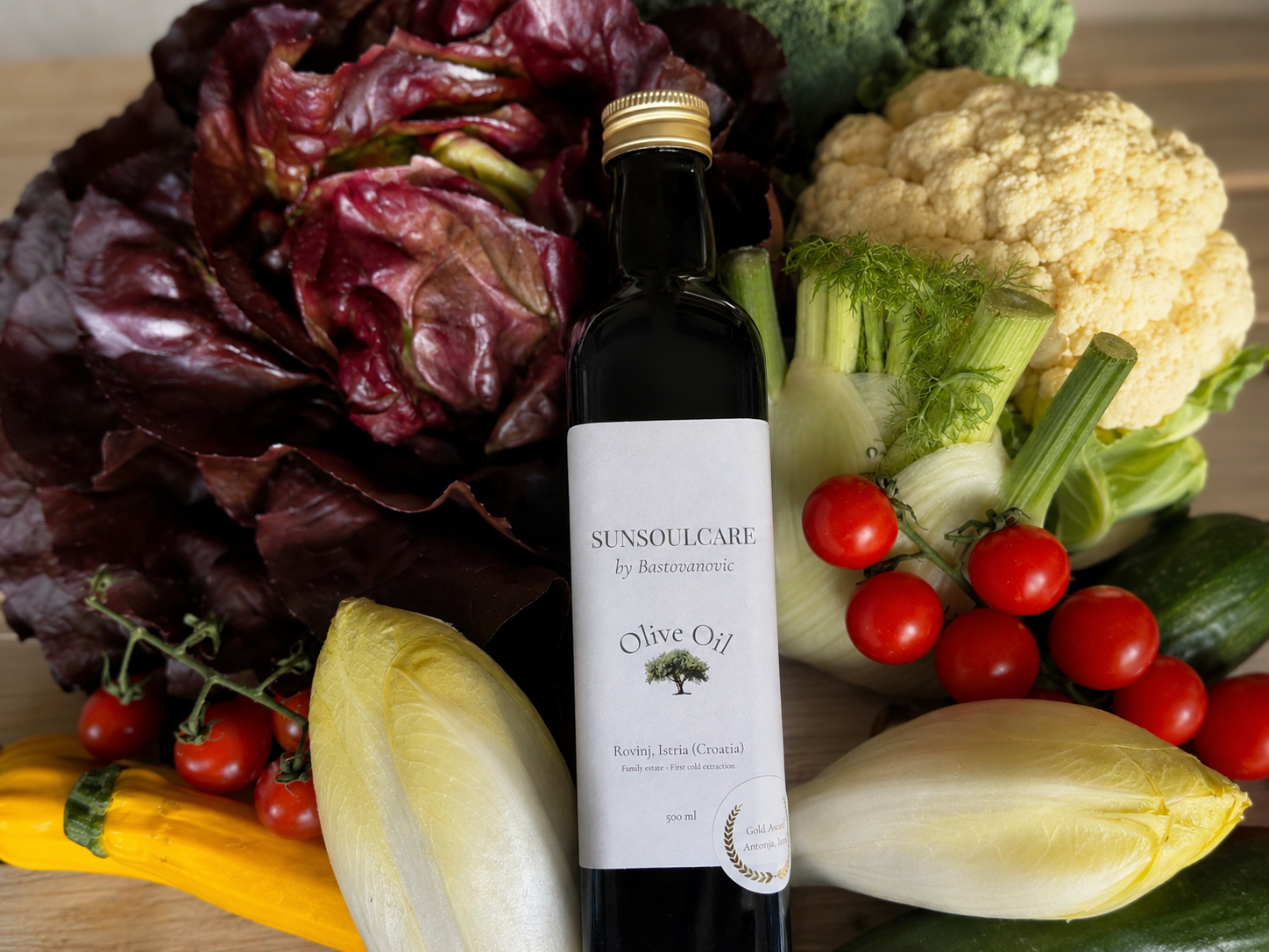 Une bouteille d'huile d'olive entourée de légumes tels que des tomates cerises, du chou-fleur, du céleri, des endives, des radis, un concombre, une courgette et une salade rouge leaves.