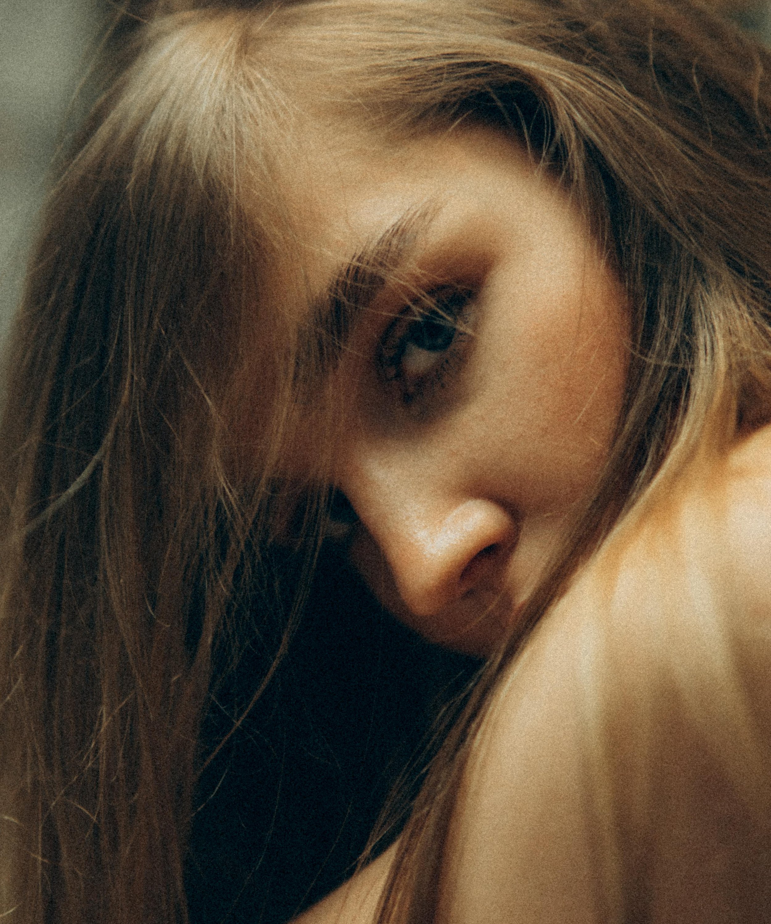 Un gros plan du visage d'une jeune femme aux longs cheveux bruns, légèrement penchée et regardant vers le bas.