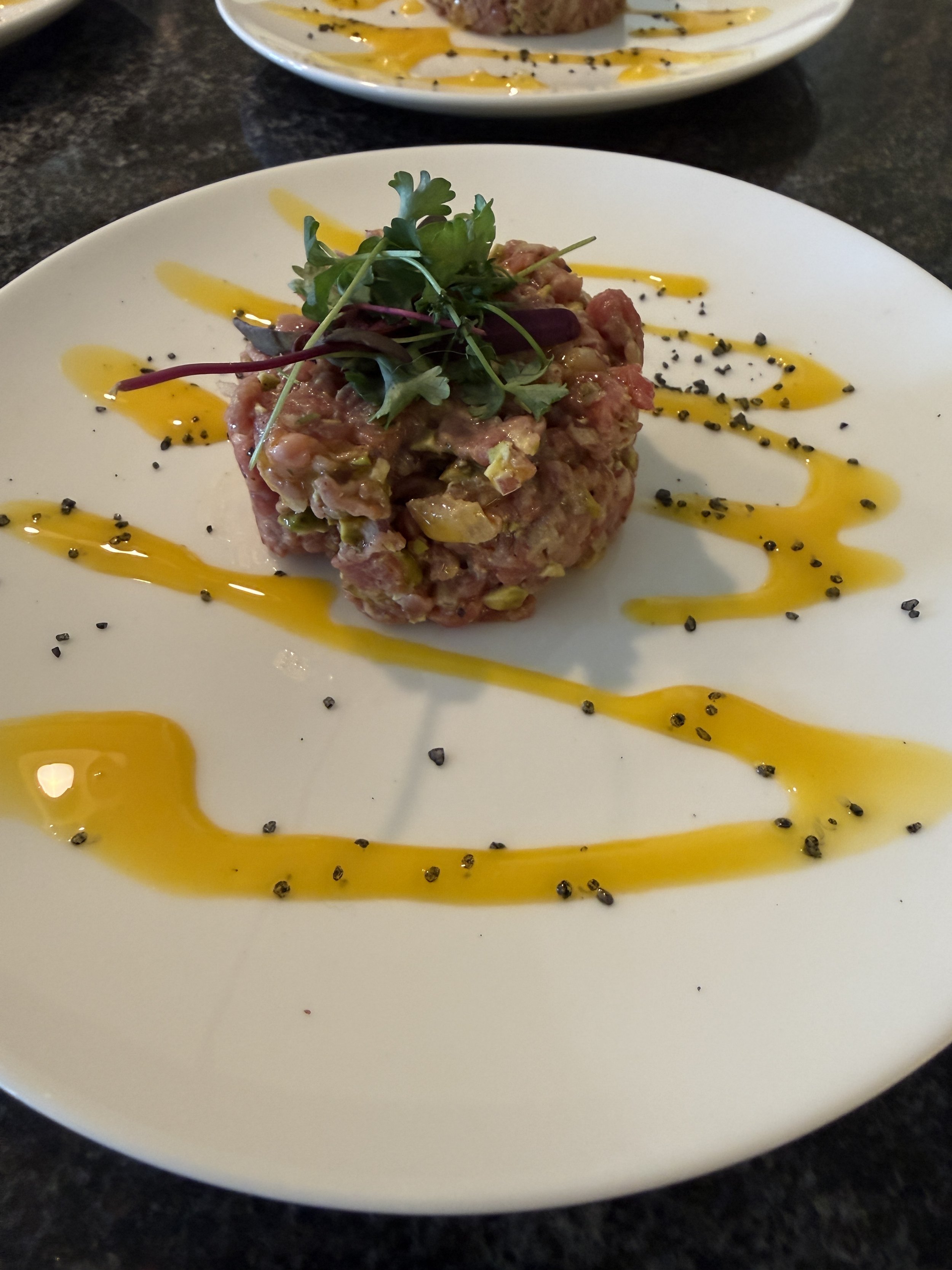 A plate with lamb tartare garnished with microgreens, egg youlk, and sprinkled with black sesame seeds.