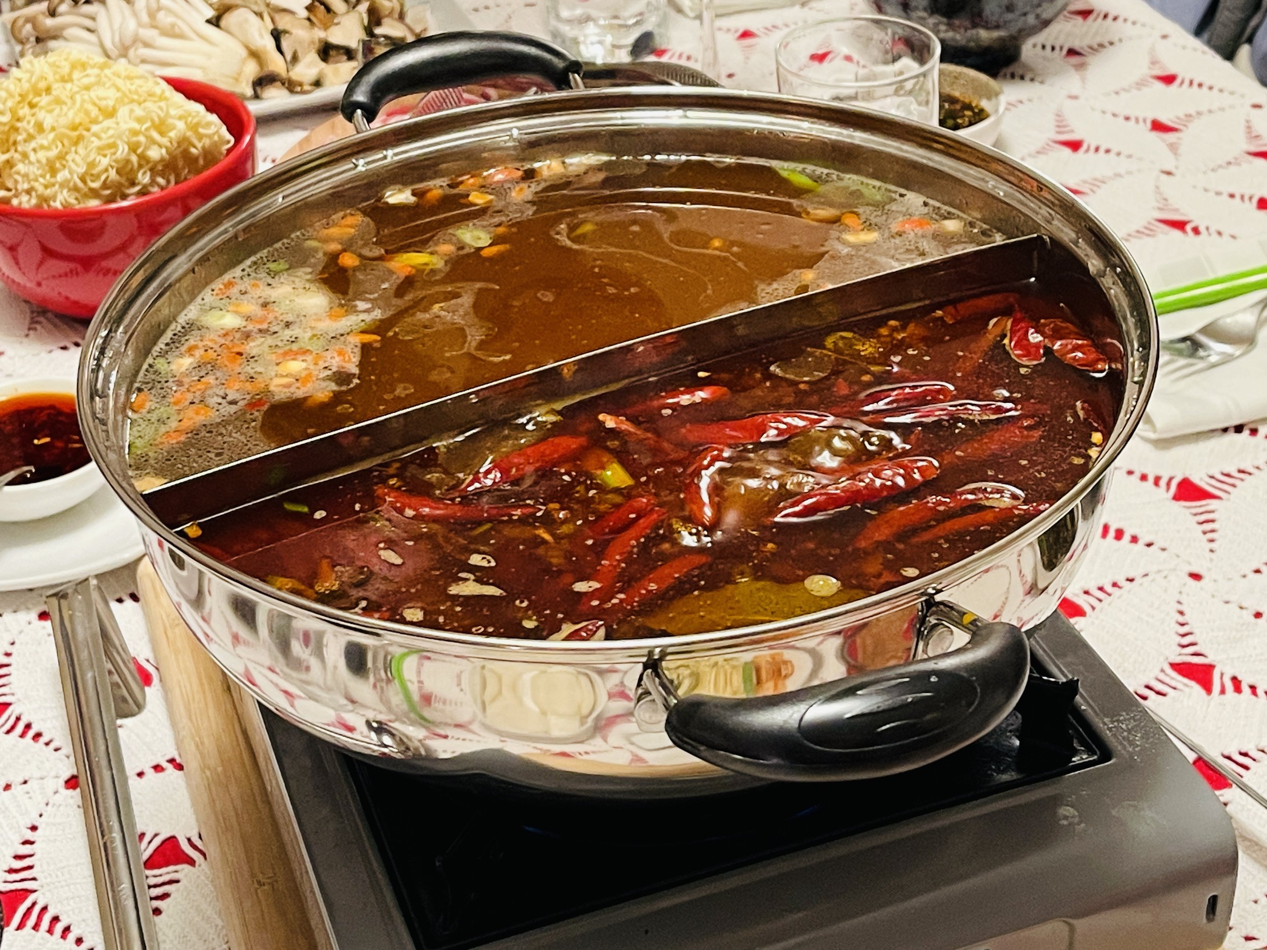 Hot pot with two separated sections of spicy and mild broth on a dining table.