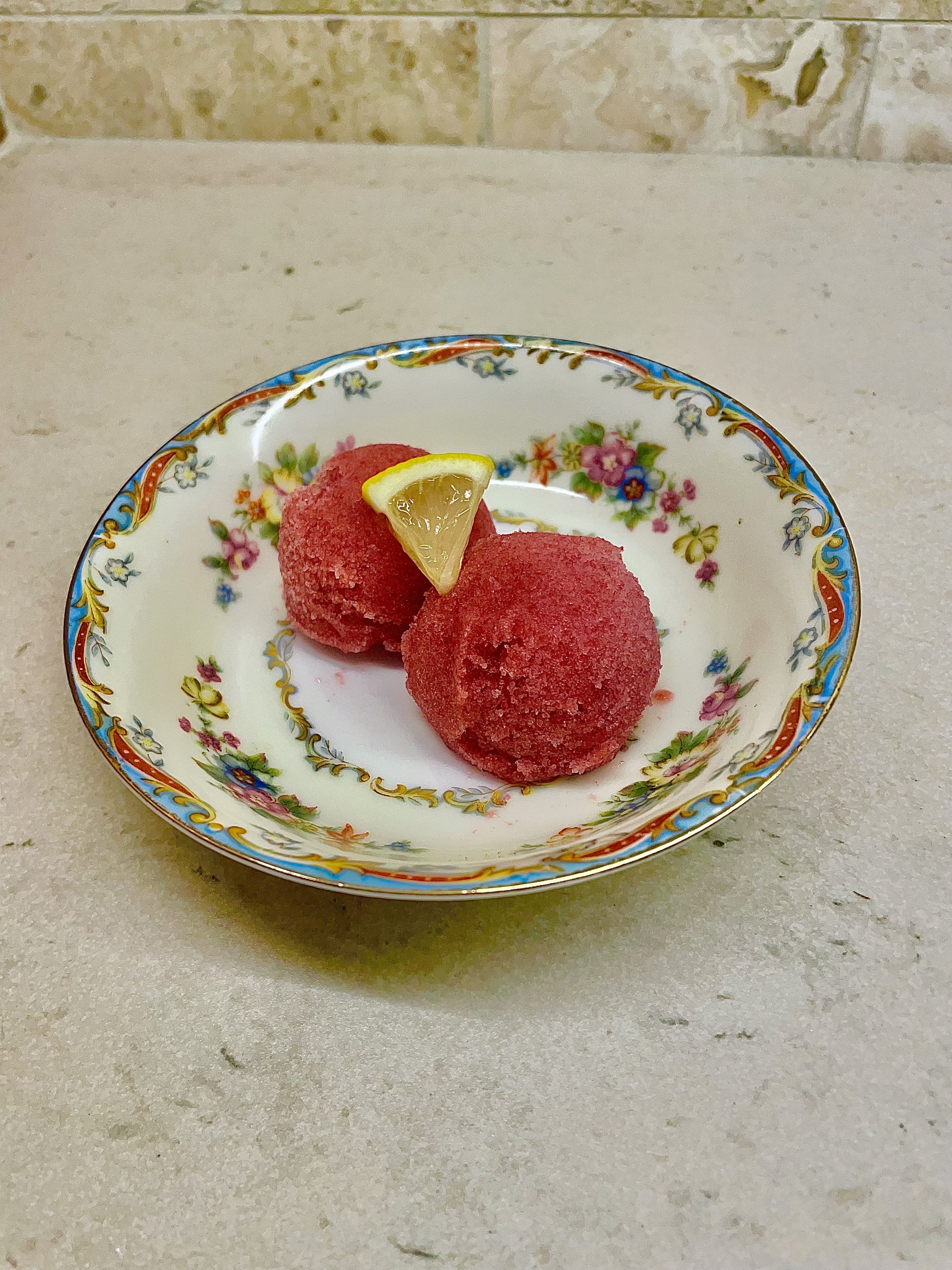 Two red snowball desserts on a decorative floral plate, garnished with a lemon wedge.