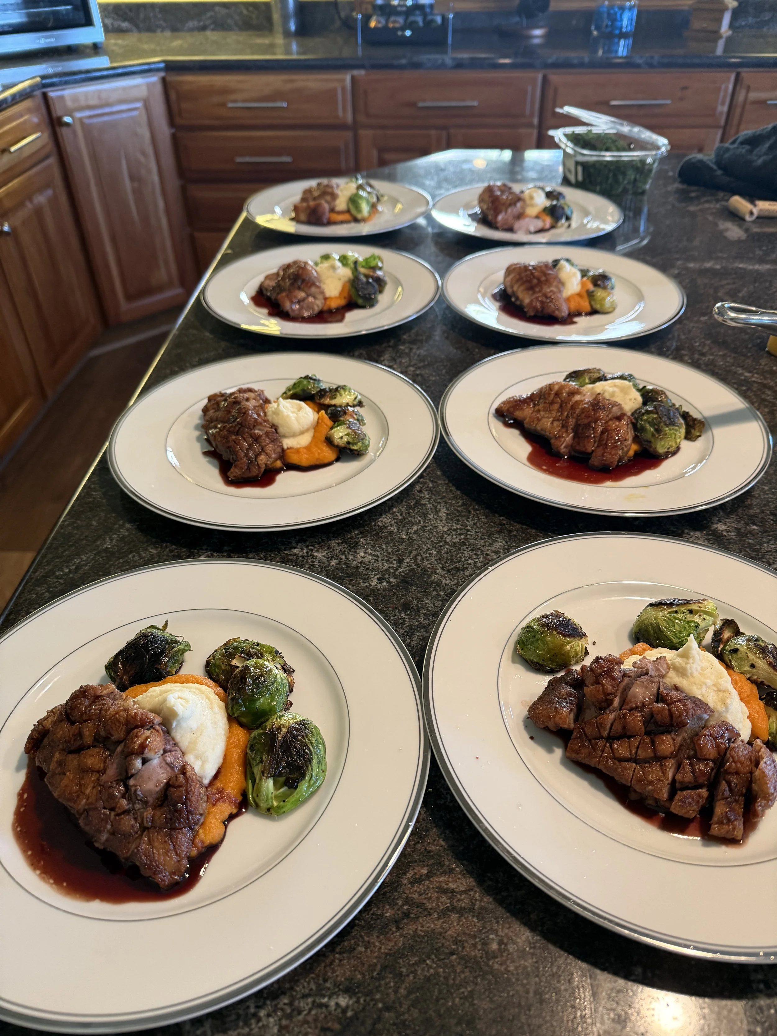 Eight plates of food on a kitchen counter, each containing grilled steak topped with sauce, roasted Brussels sprouts, and mashed potatoes.