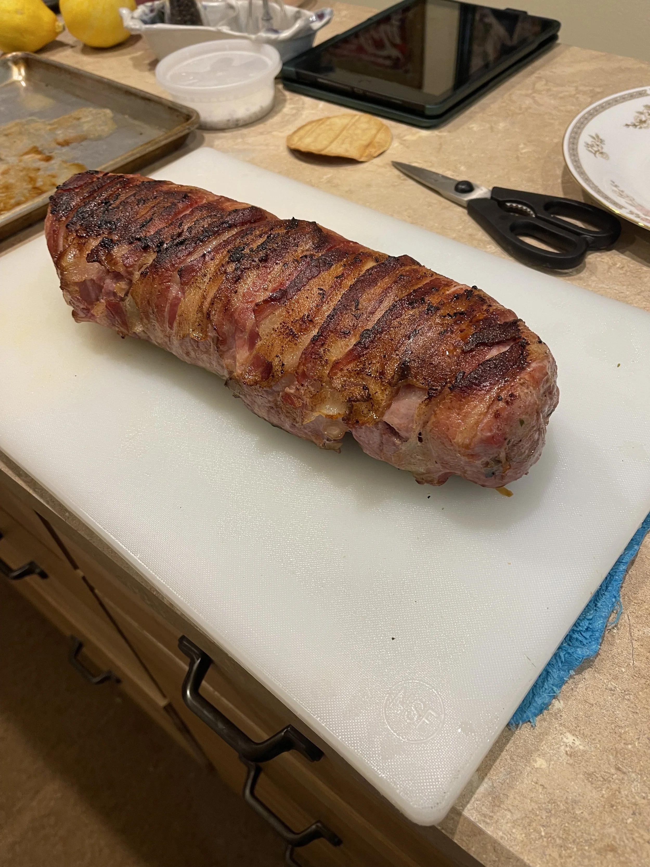 Cooked bacon-wrapped meatloaf on a white cutting board in a kitchen.