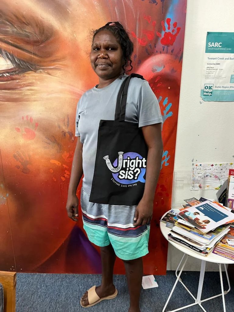A young Aboriginal woman wearing a black 'U Right Sis?' tote bag and smiling.