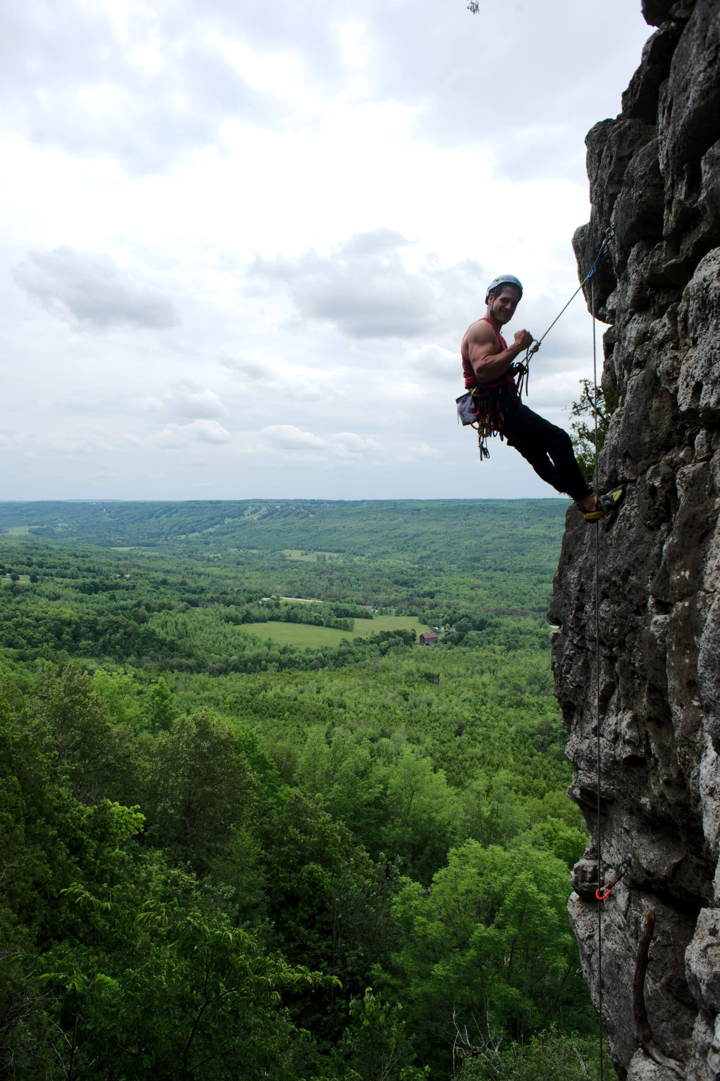 Person rock climbing on a steep cliffside with a lush green landscape in the background.