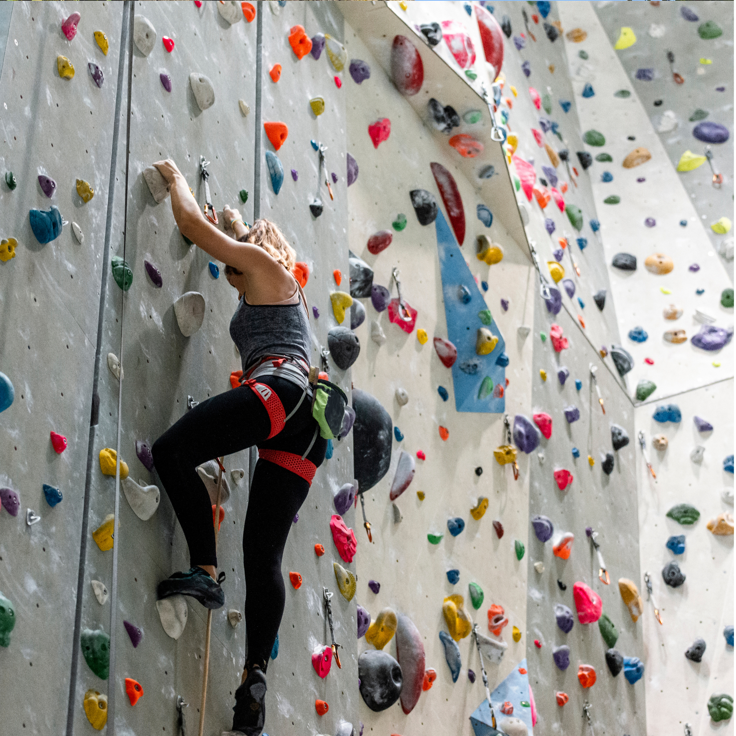 A woman climbing an indoor rock wall with colorful holds.
