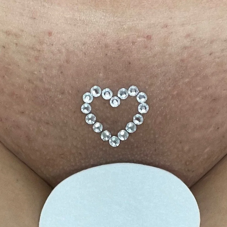 Close-up of a navel piercing with rhinestones arranged in the shape of a heart.