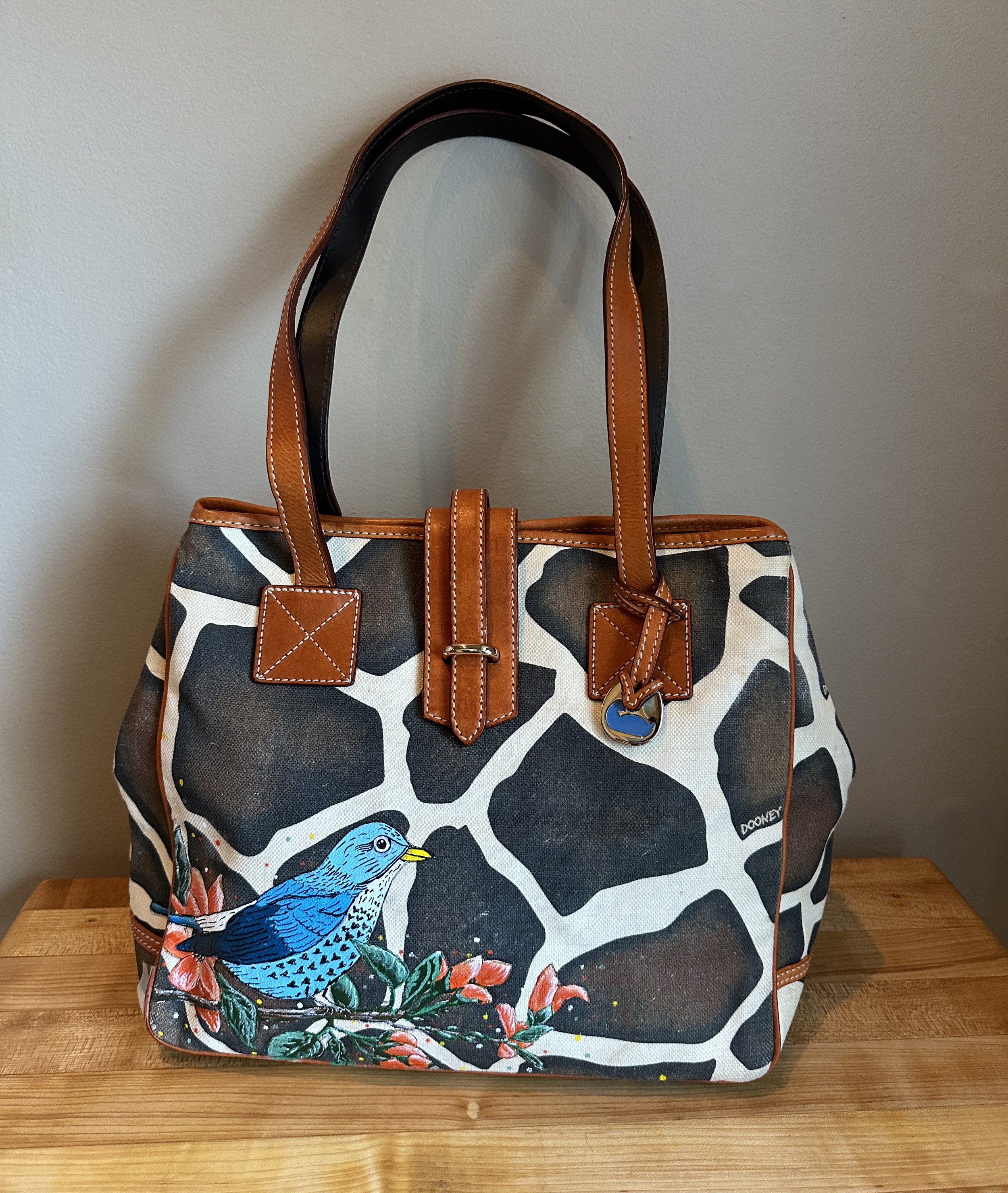 Authentic vintage Dooney & Bourke purse, upcycled with a hand-painted bird design that adds character while covering a small surface flaw. Unique, practical, and reimagined with care.