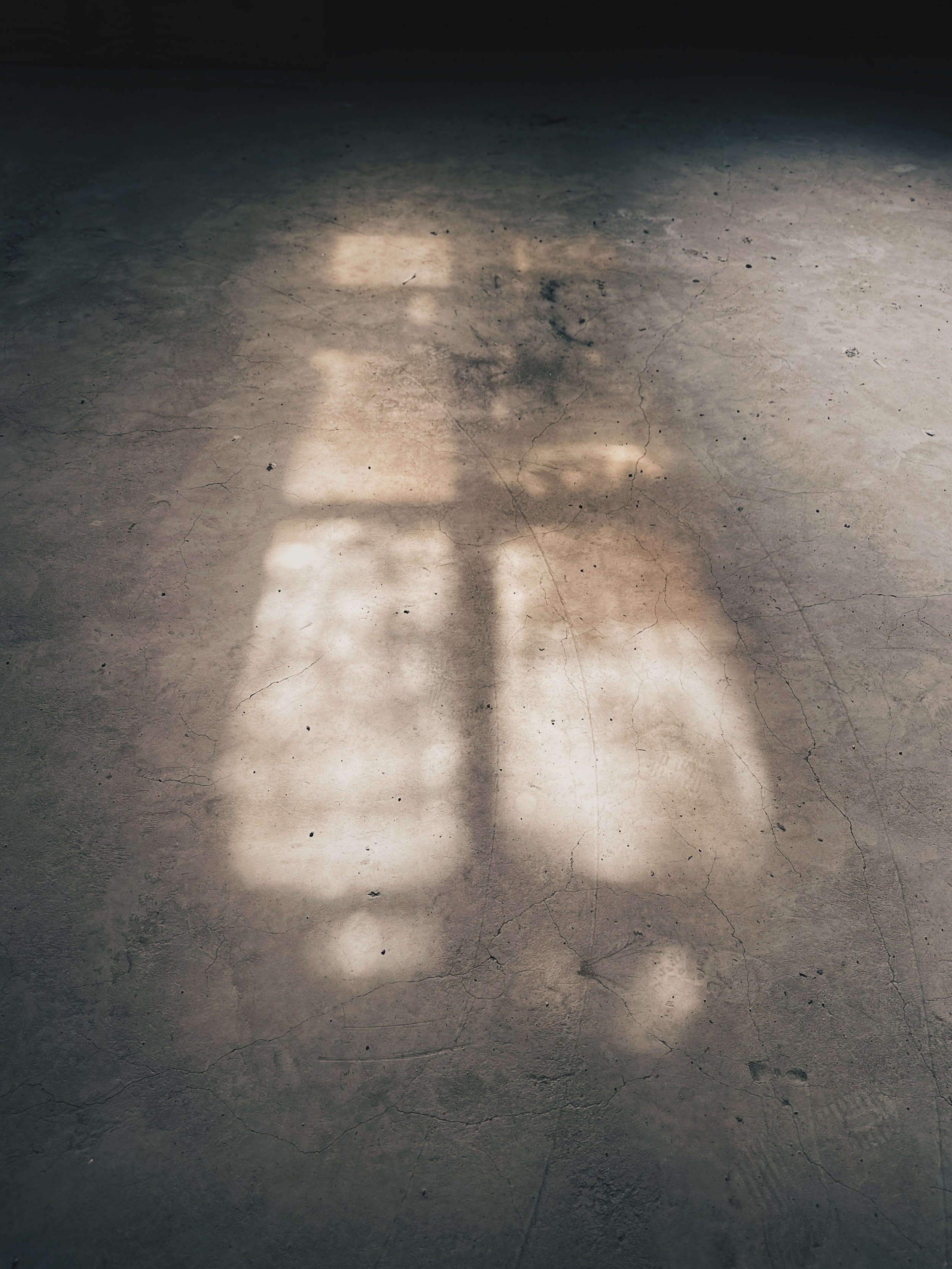 A cracked concrete floor with patchy spots of sunlight and shadows.