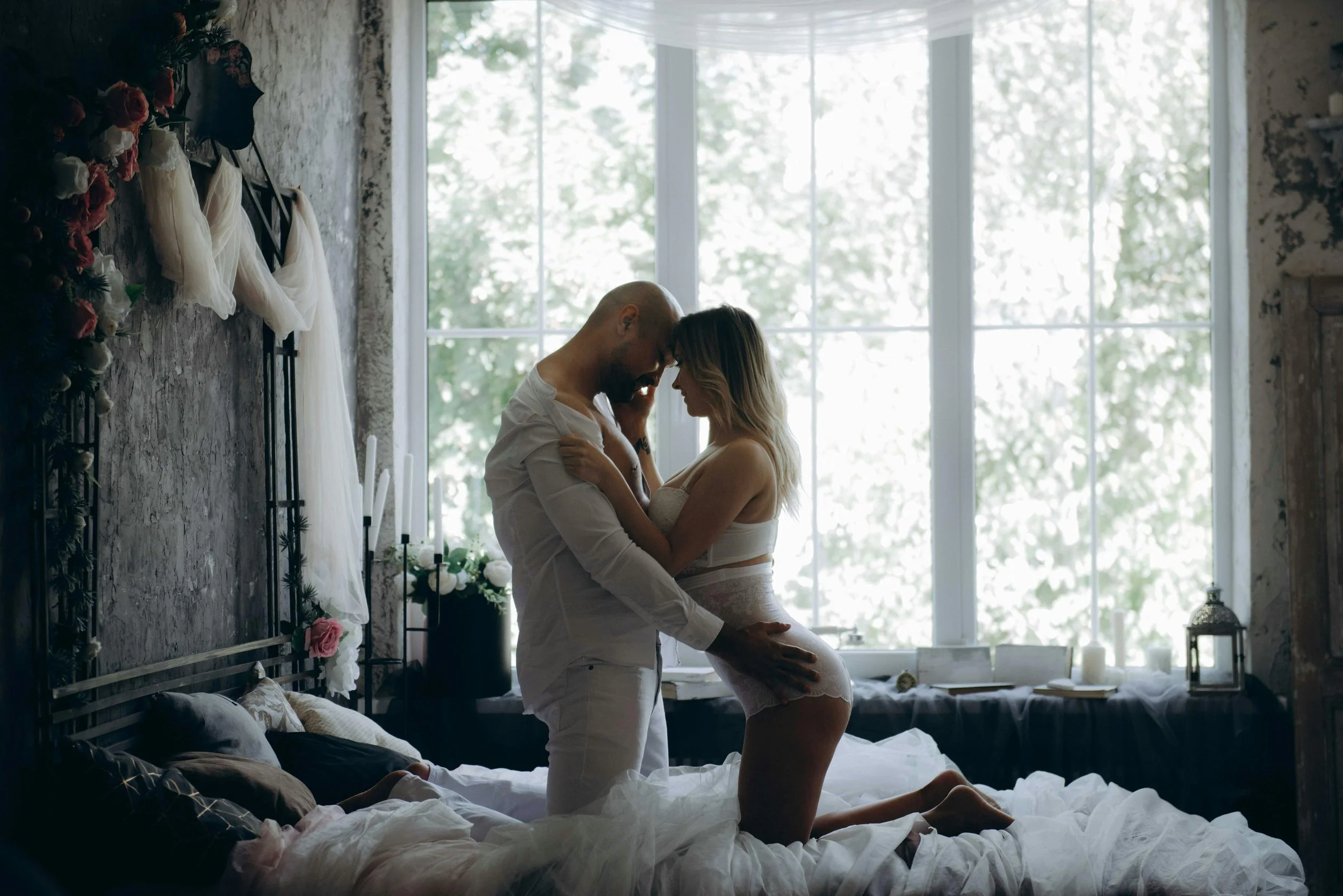 Una pareja en una habitación con luz natural, ambos semidesnudos, en una pose íntima y afectuosa.