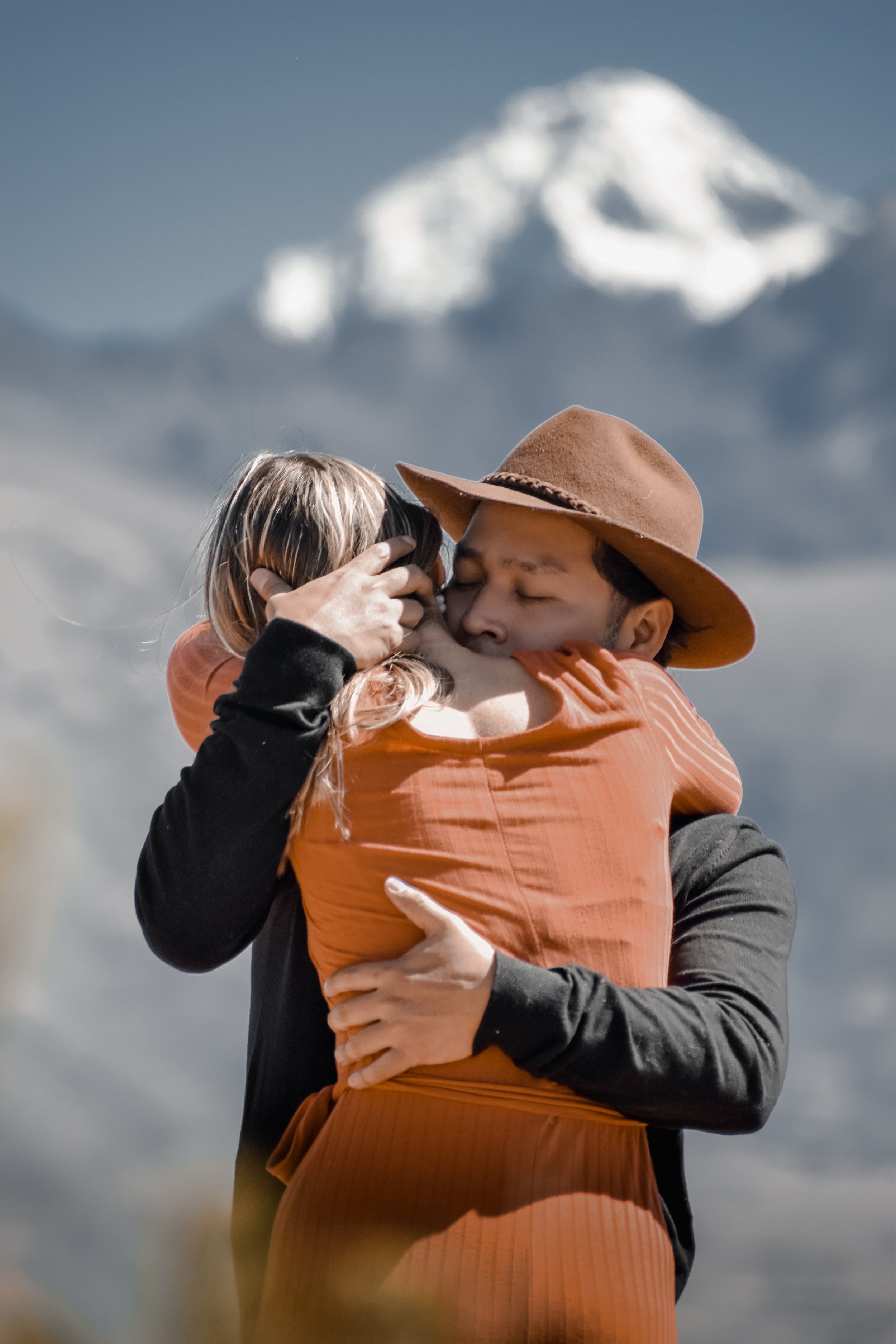 Una pareja abrazándose en un paisaje montañoso con una cumbre nevada en el fondo.