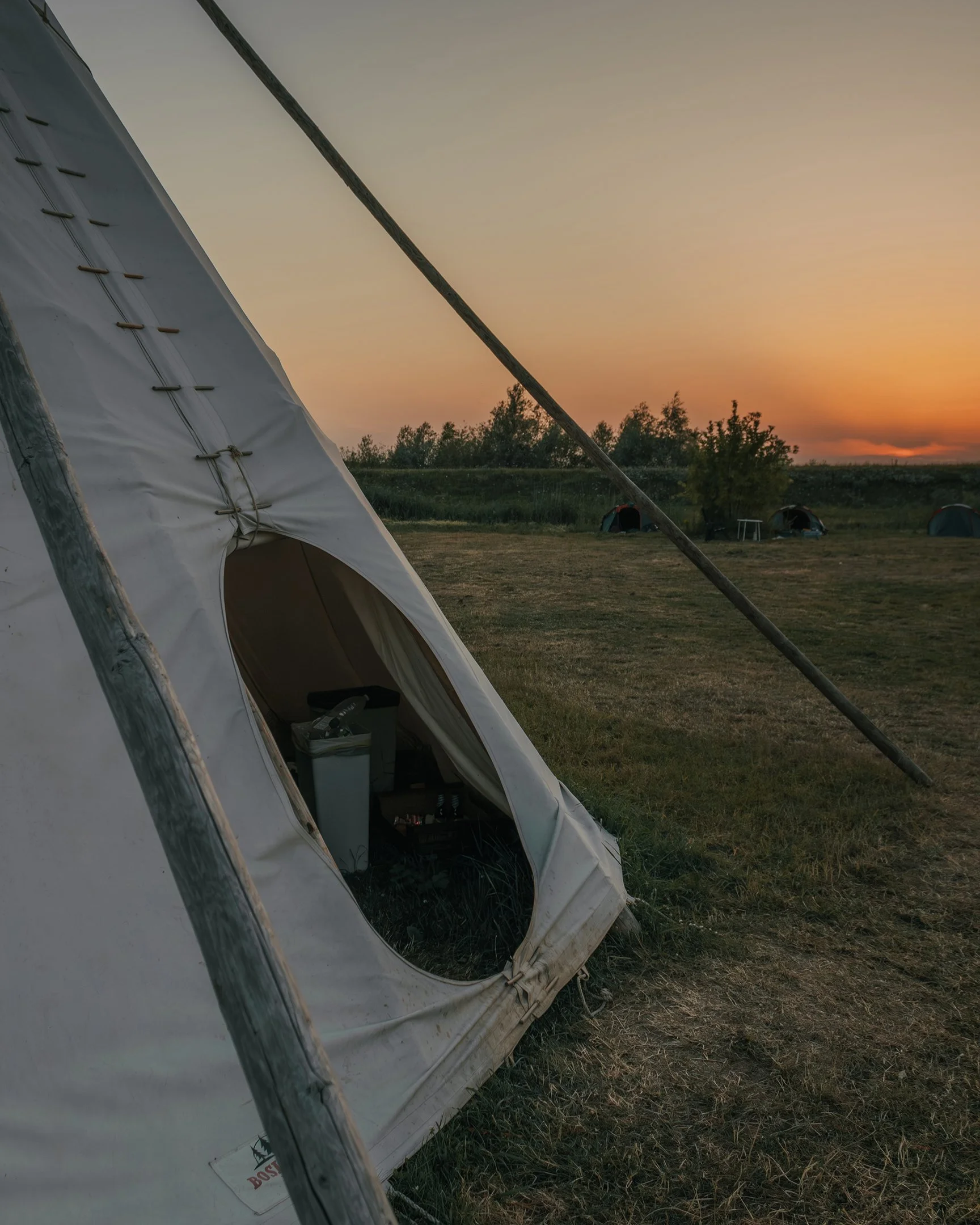 A camping tent set up on a grassy field at sunset with other tents visible in the background.