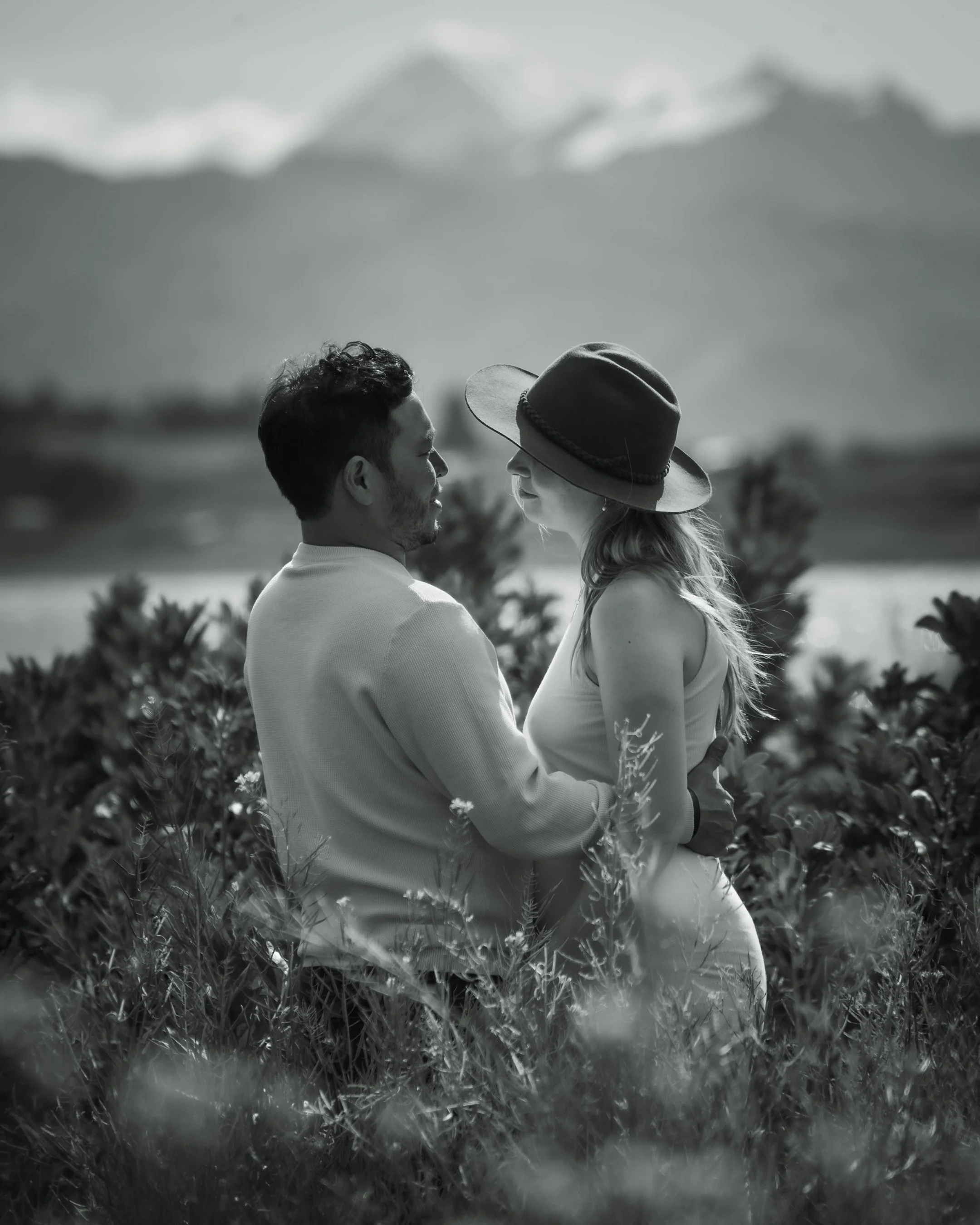 Una pareja abrazada en un campo con montañas al fondo, en blanco y negro.