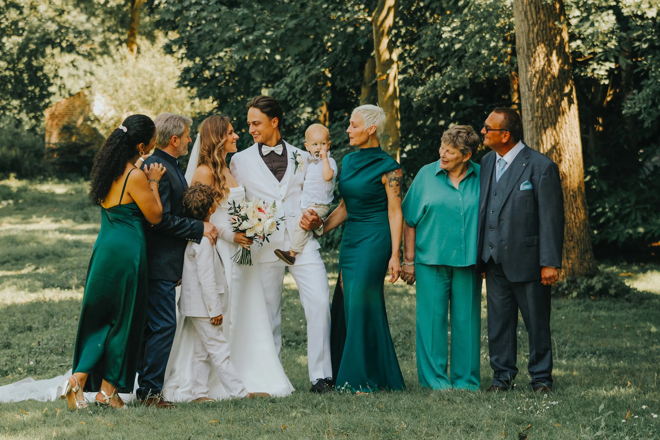 Grupo de personas en una boda al aire libre, incluyendo a los novios y familiares, rodeados de árboles
