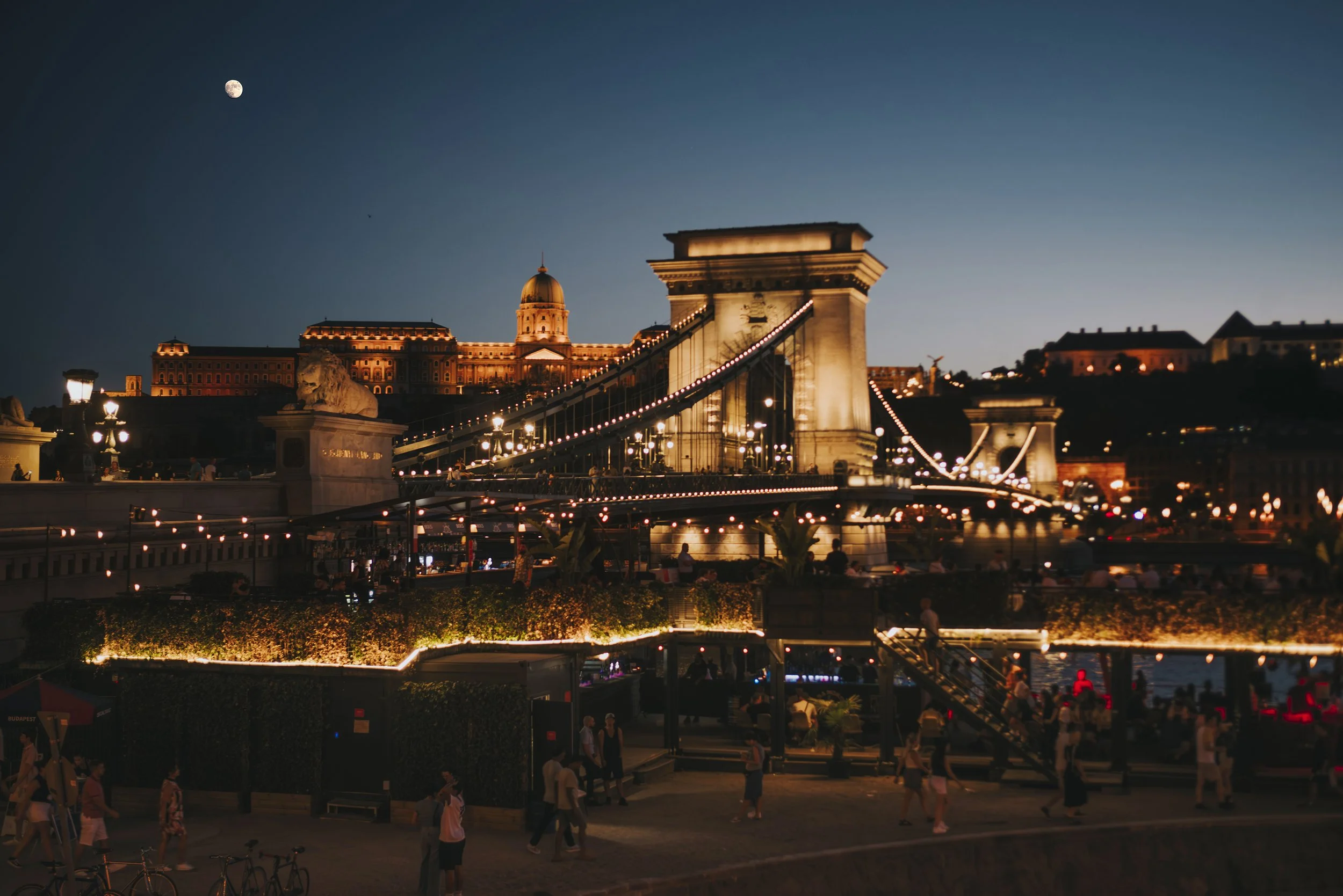 Puente de las Cadenas en Budapest en la noche, iluminado y con la luna visible en el cielo.