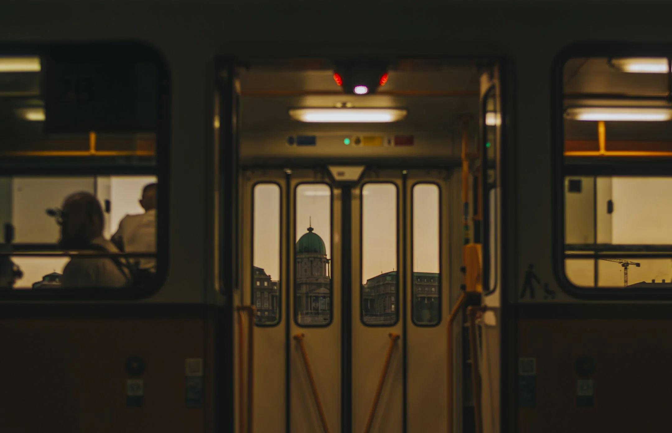 Interior of a tram or bus with a view through the front doors showing a cityscape and a building with a green dome at sunset.