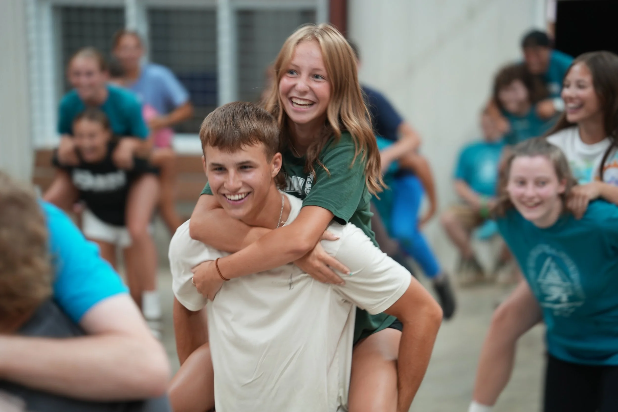 Group of children playing and having fun indoors, with a girl riding on a boy's back, all smiling and enjoying the activity.
