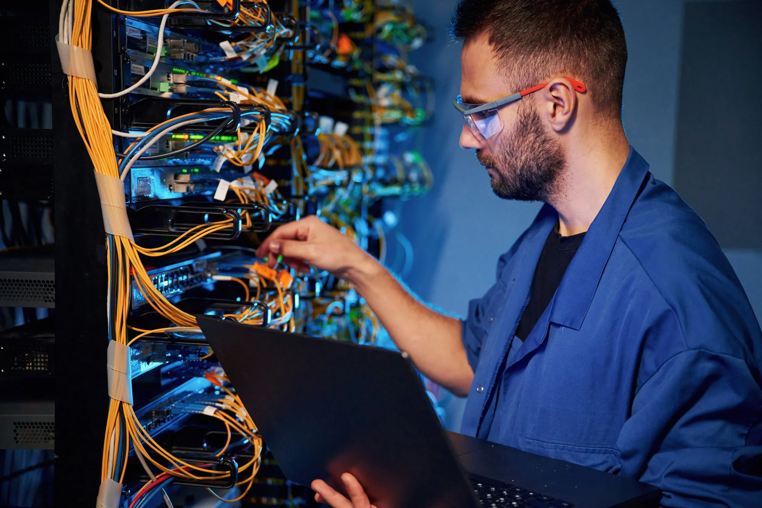Technician working on a server rack with numerous network cables and blinking LED lights.