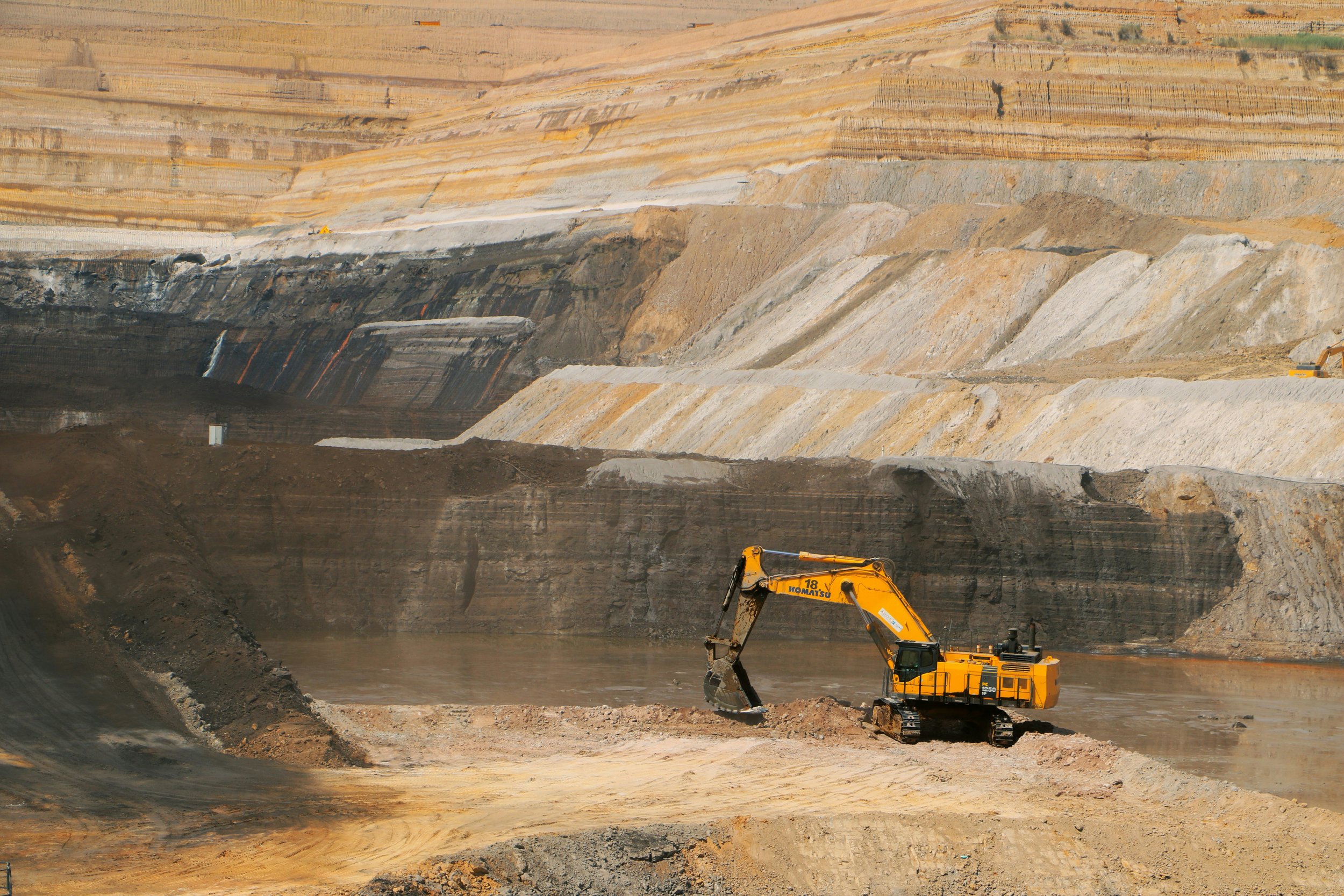 A large open-pit mining operation with an excavator working on the excavated earth surrounded by colorful layers of rock and soil.
