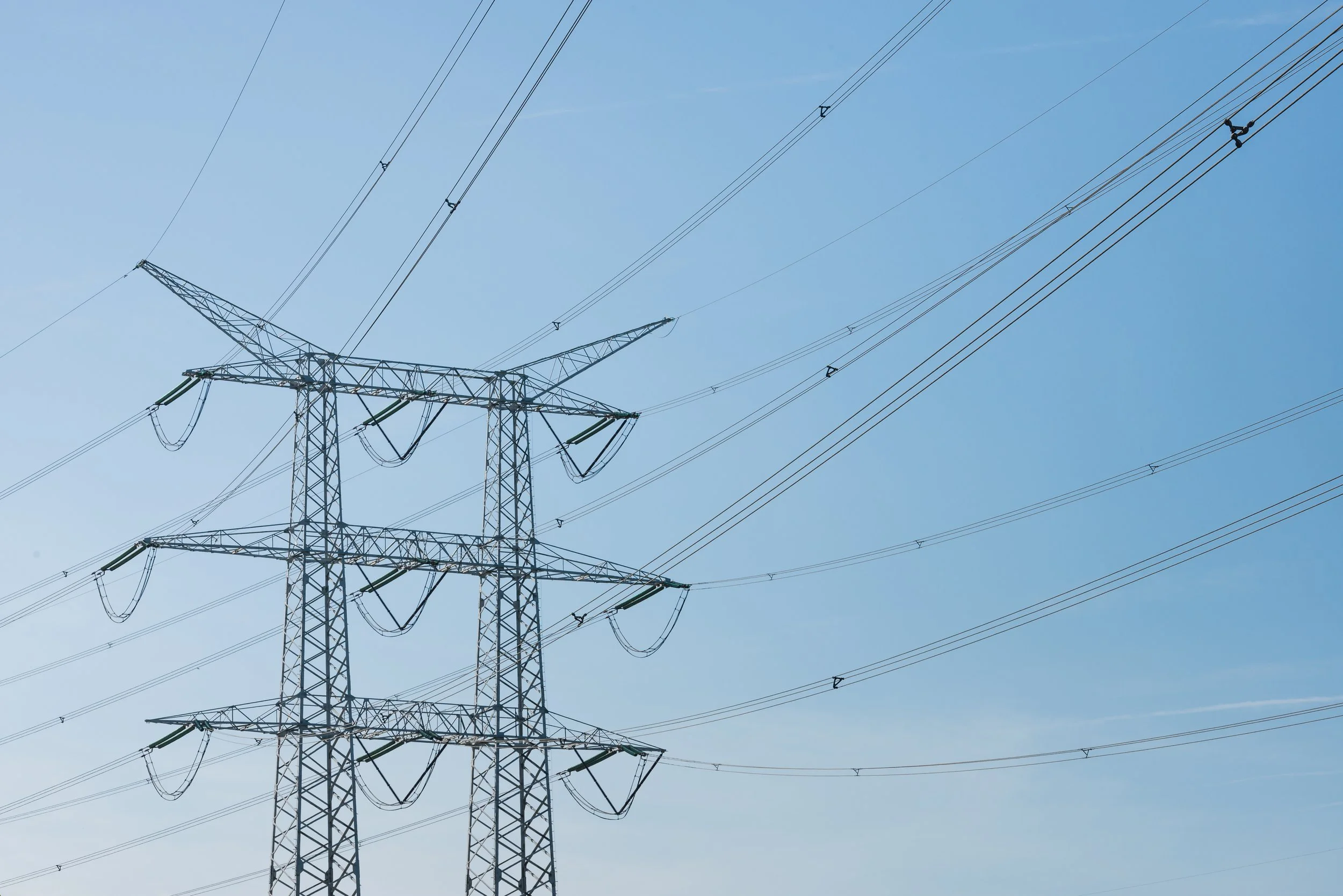 Large electrical transmission towers with high voltage power lines against a clear blue sky.