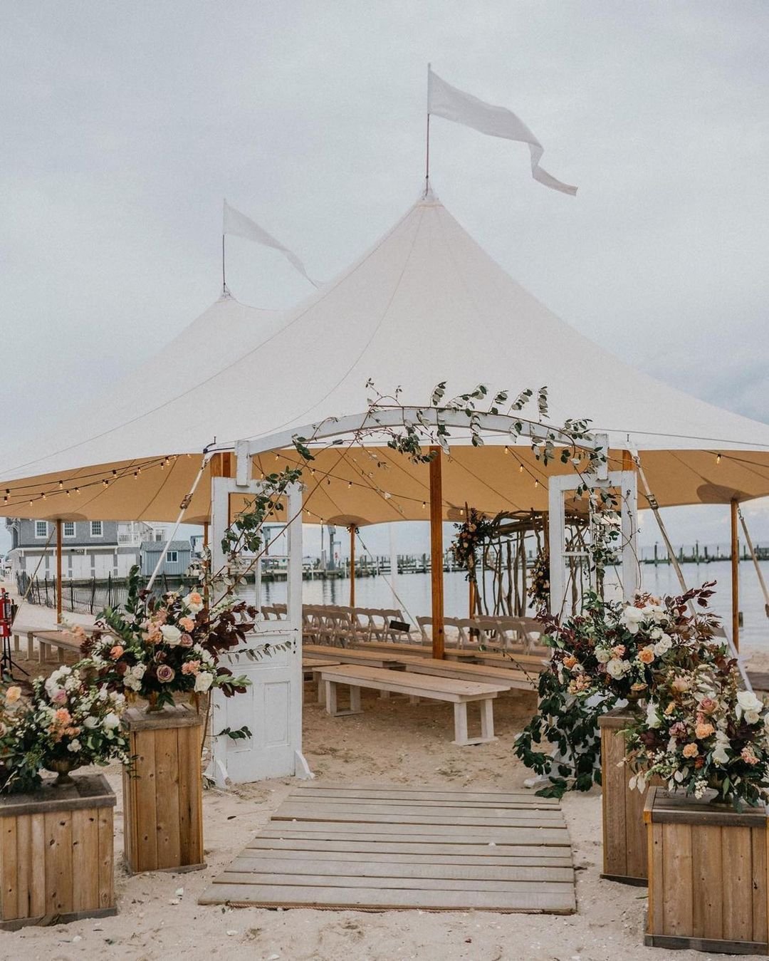 Step into elegance with this rustic-chic entrance! Vintage doors open up to a breathtaking beach ceremony, perfectly framed by the timeless beauty of Sperry Tent. The blend of natural elements and coastal charm creates an unforgettable first impressi