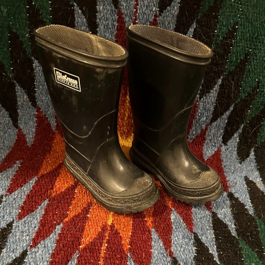 Pair of black rubber rain boots standing on a multicolored textile background.
