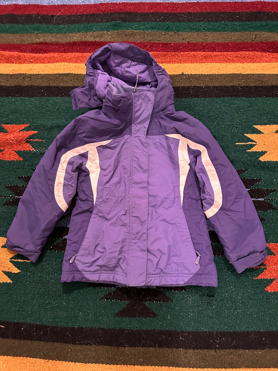 A purple LL Bean winter jacket with a hood, lying on a colorful striped rug.