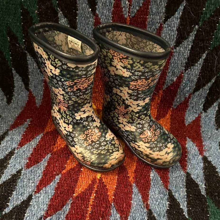 Pair of rain boots with floral pattern on a multicolored, geometric-patterned rug.