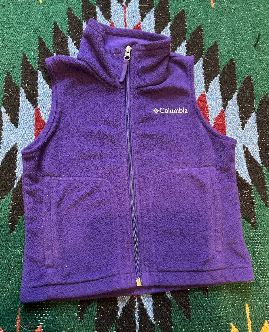 A purple Columbia fleece vest with a zippered front, placed on a colorful patterned rug.