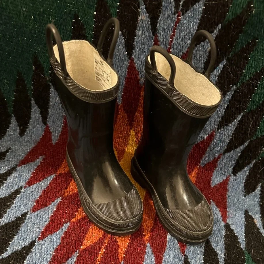Pair of black rubber rain boots placed on a colorful, patterned carpet.