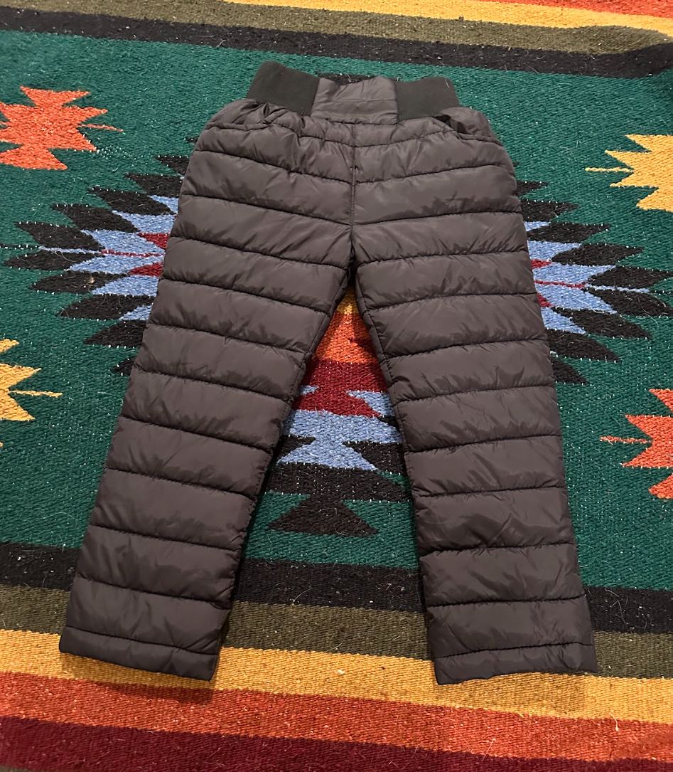 A pair of black puffer pants lying on a colorful southwestern patterned rug.
