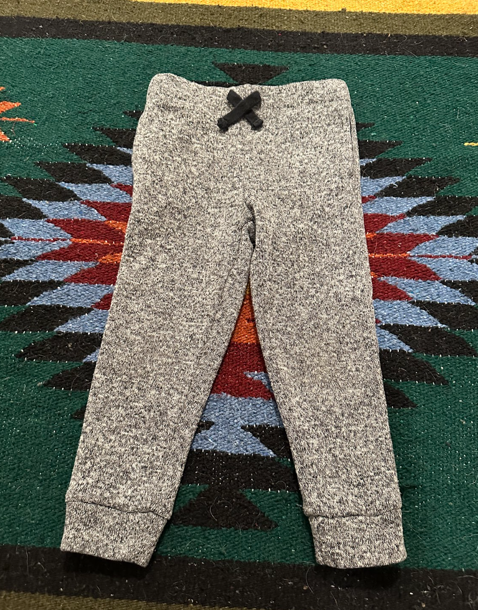 Gray sweatpants with a black drawstring lying on a colorful southwestern-style rug.