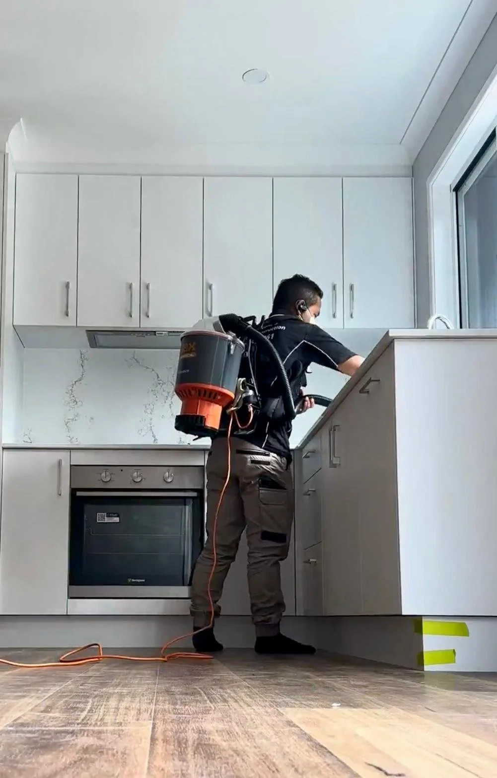 A pest control professional with a backpack sprayer inspecting a kitchen cabinet.