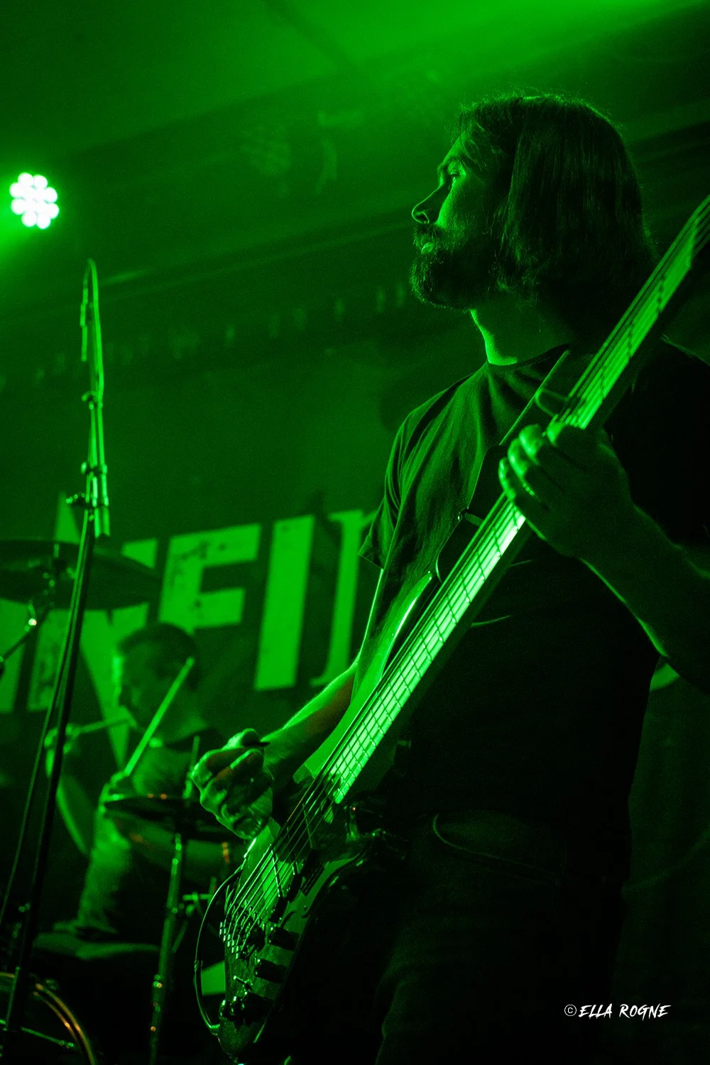En mann spiller bassgitar på en scene opplyst med grønn belysning.