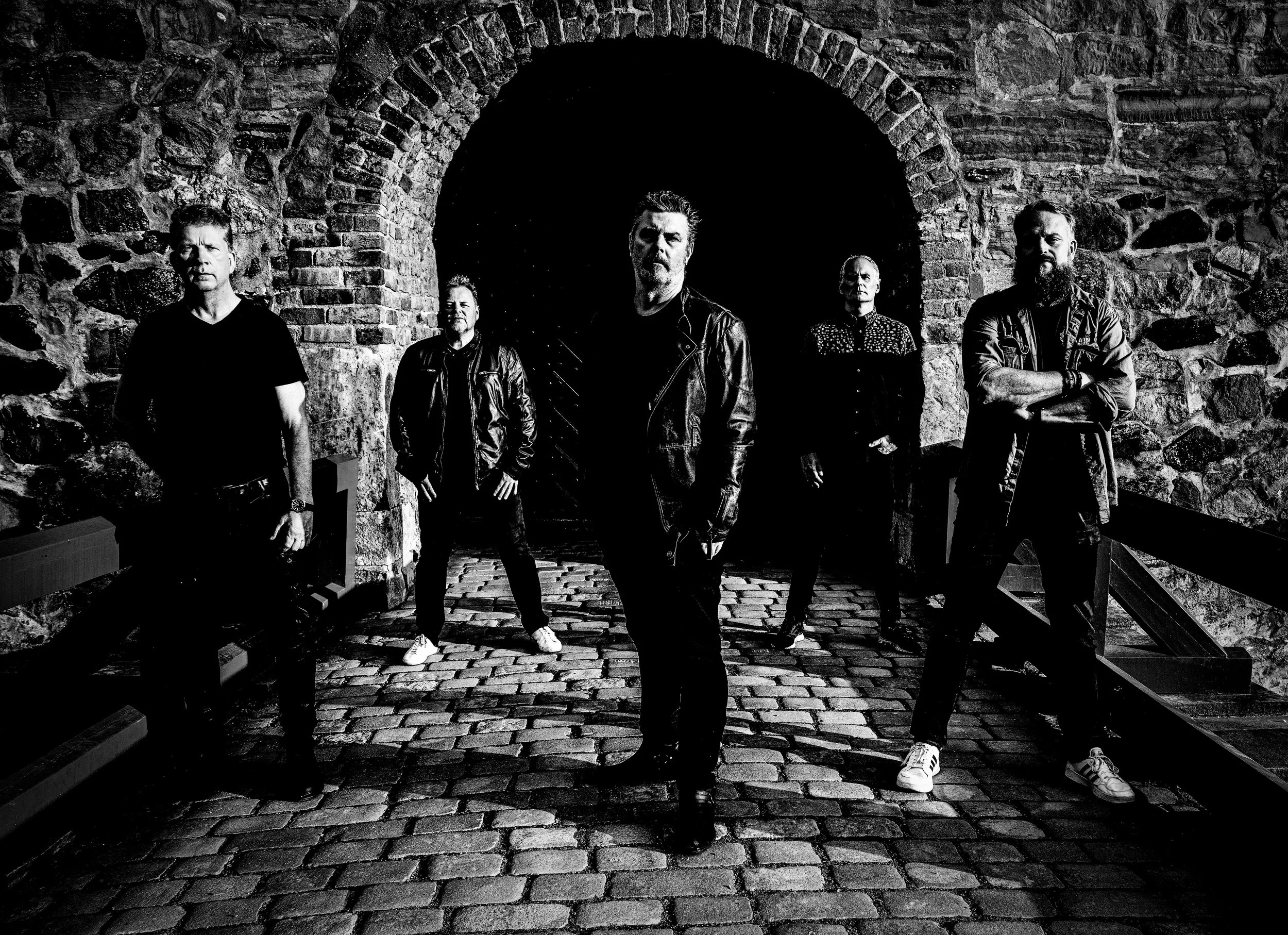 Fem menn står foran en steinbuet inngang på en bro, kledd i mørke klær, protesterende i svart-hvitt.