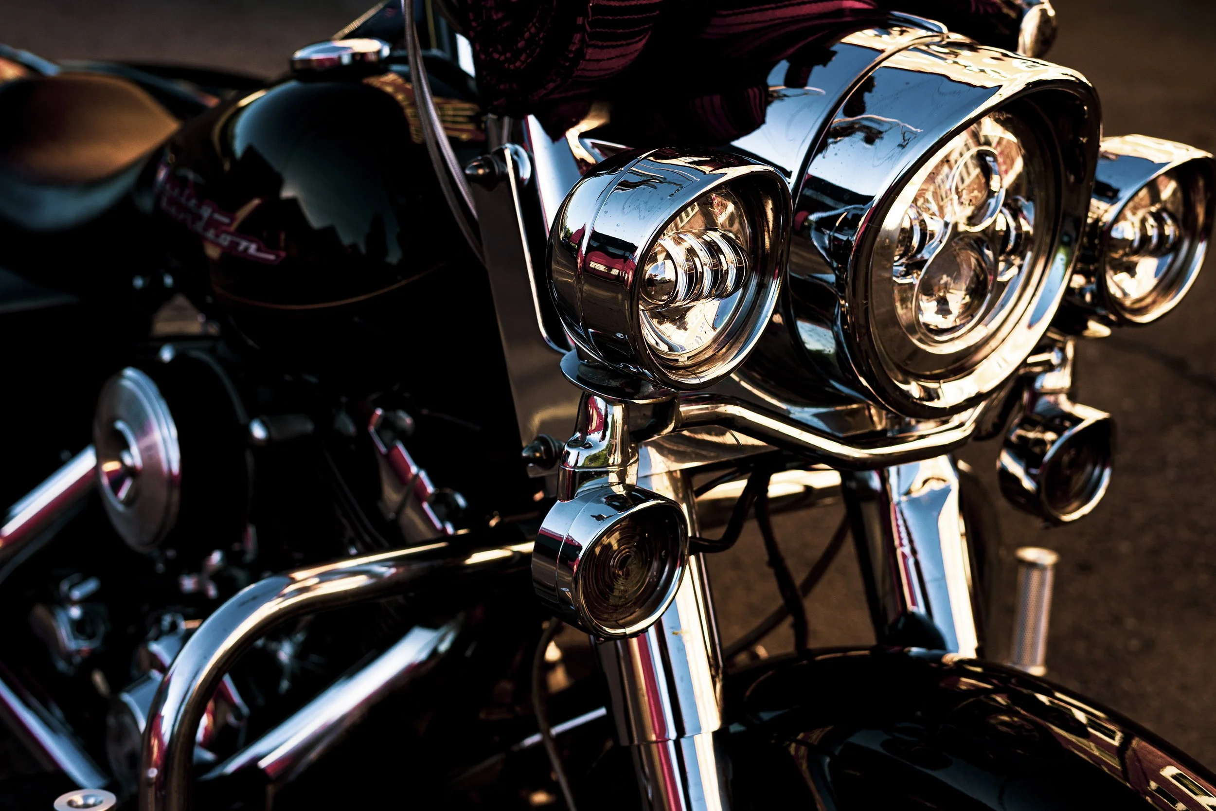Nærbilde av fronten på en svart motorsykkel med blanke chrom- og metallkomponenter, inkludert frontlykter og deler av styret.