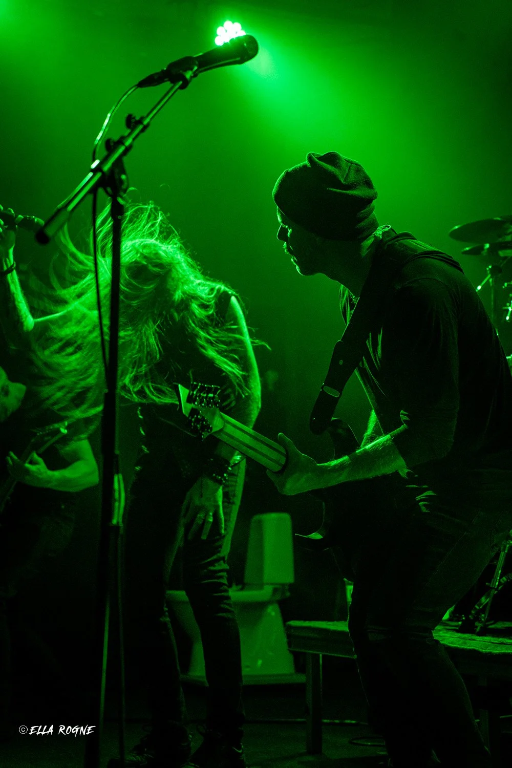 To musikere spiller gitar på en scene opplyst med grønt lys.