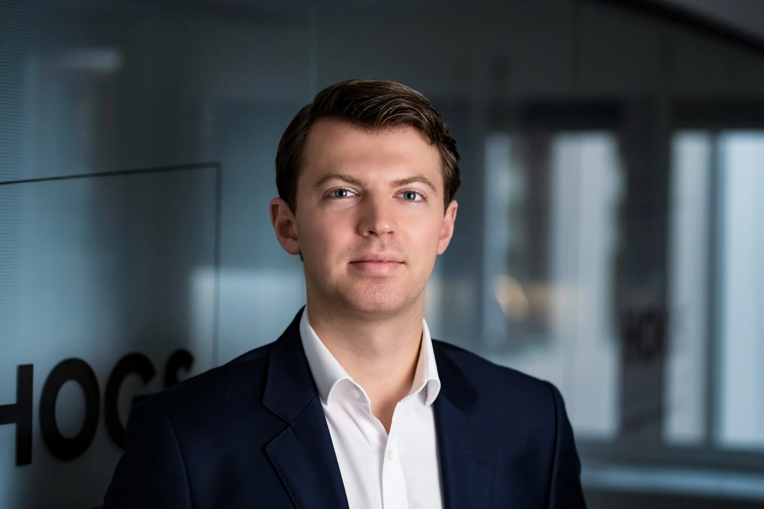 En mann i dress står i en korridor med glassvegger.