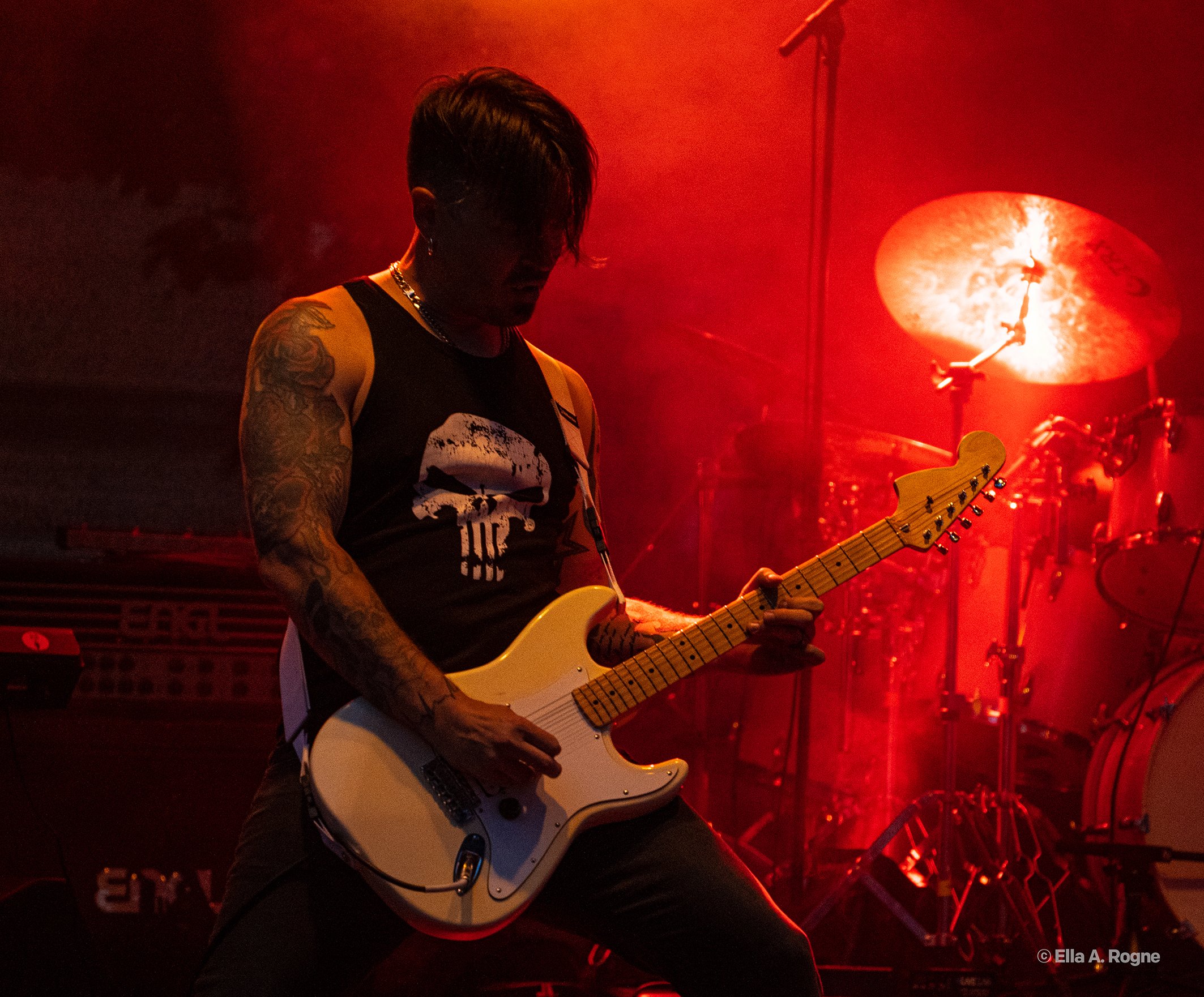Gitarist spiller på scene med rødt lys bakgrunn.