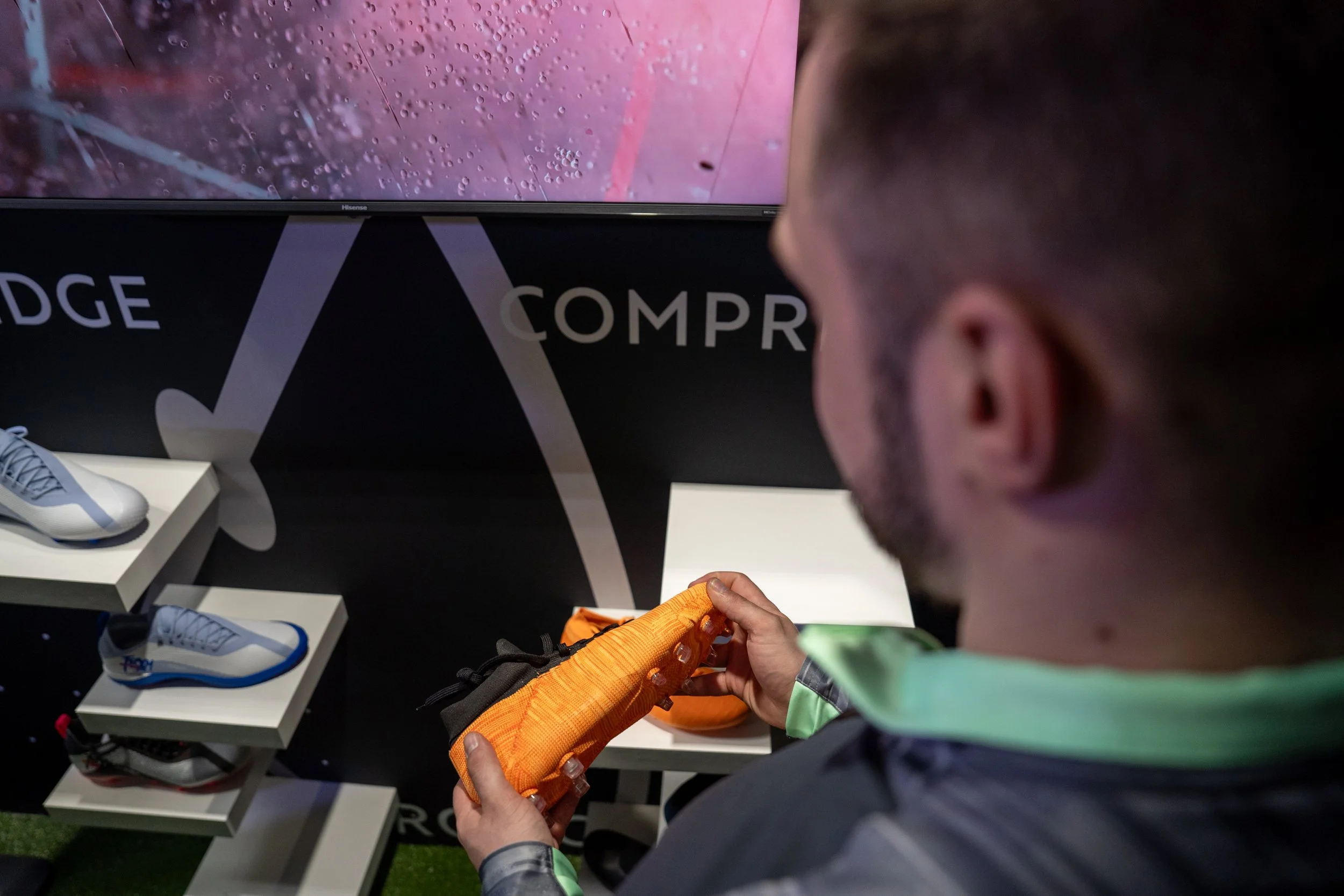 Un homme regarde une chaussure de sport orange lors d'une exposition ou d'un magasin de sport