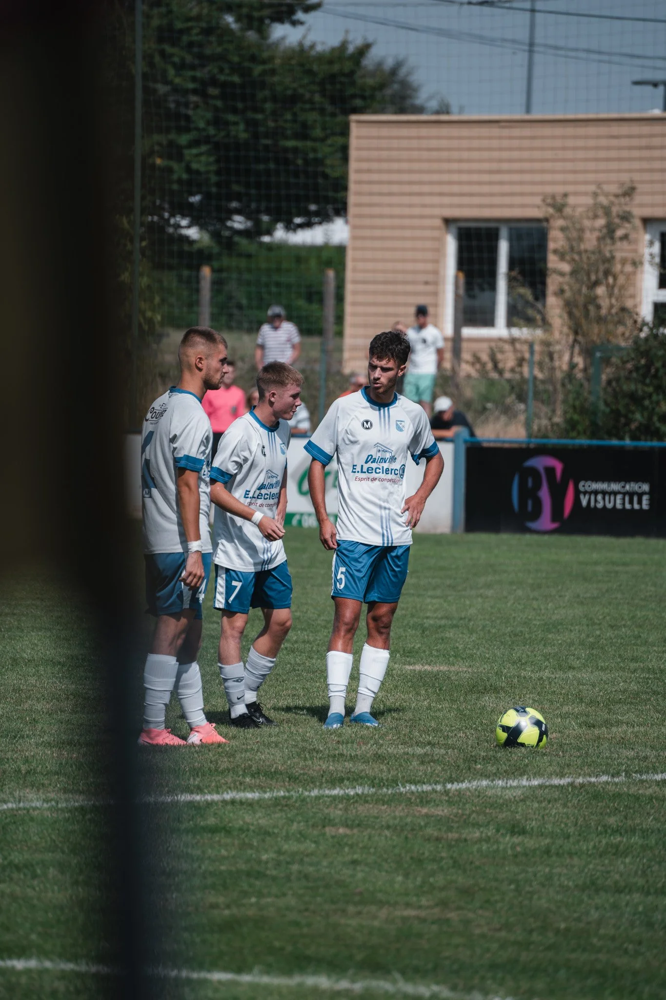 Quatre joueurs de football en uniformes blancs et bleus se préparent pour un coup franc sur un terrain de football.
