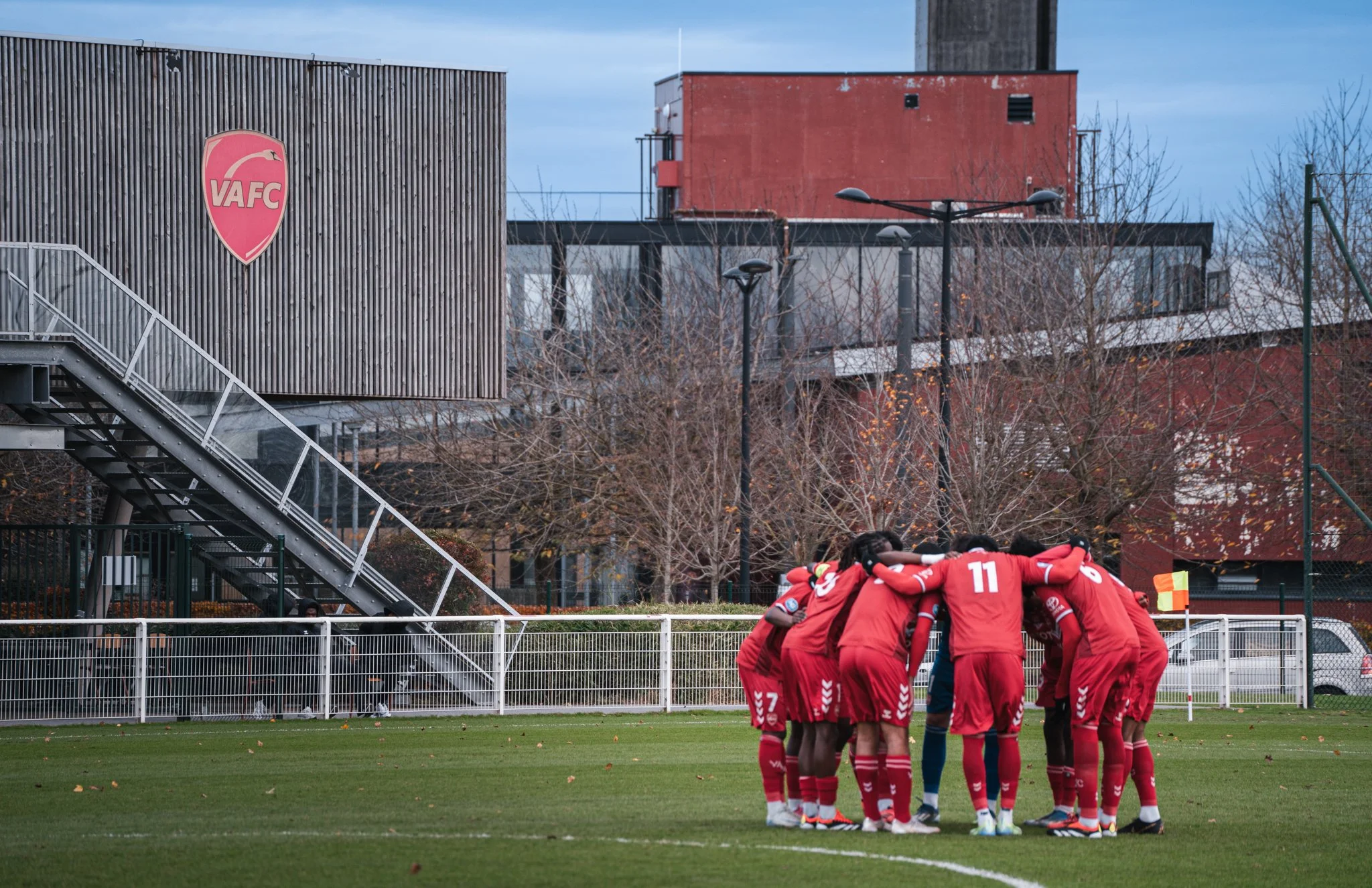 Une équipe de football en rouge se rassemble en cercle sur le terrain avant le match
