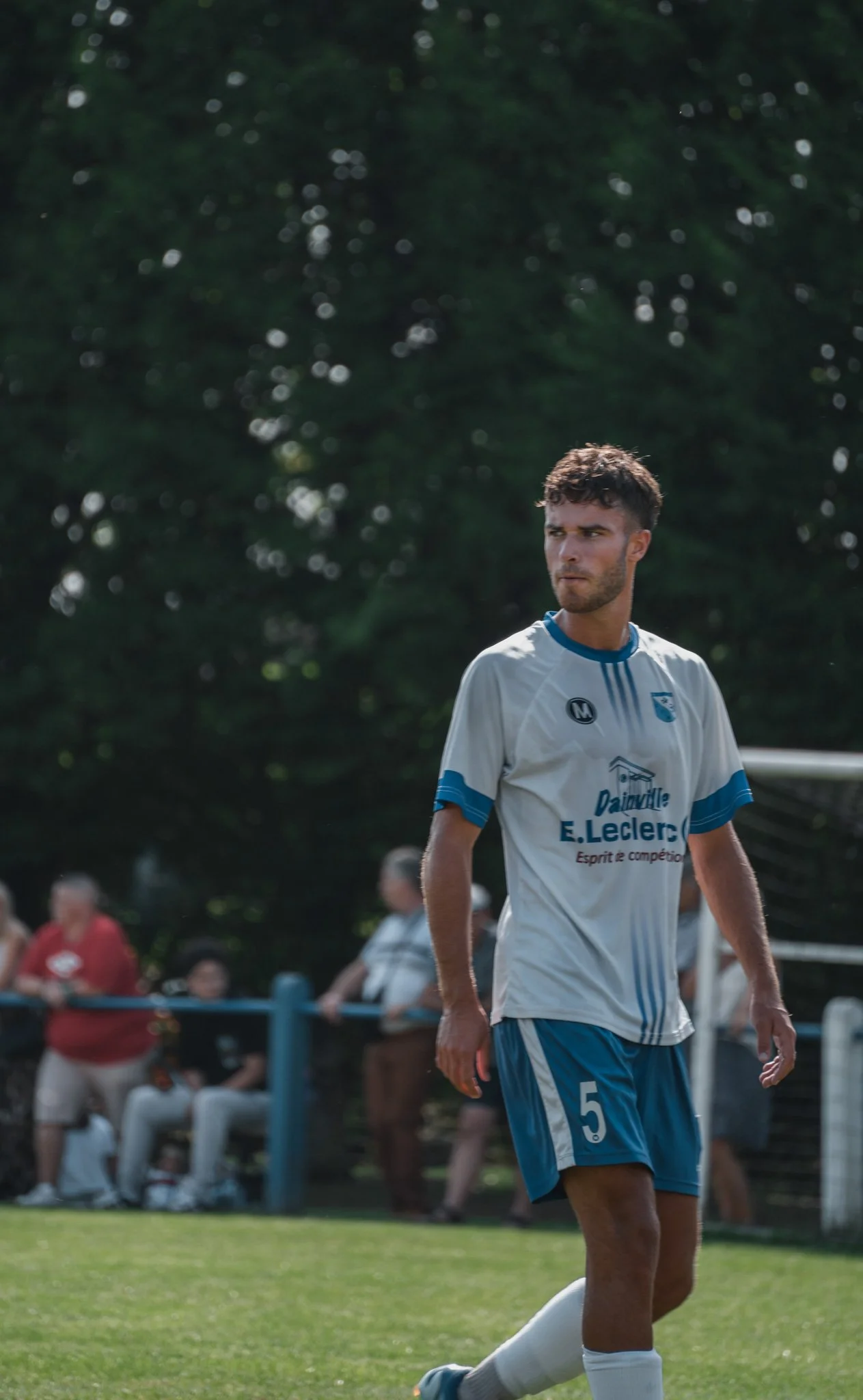 Jeune joueur de football sur le terrain, portant un maillot blanc et bleu avec le numéro 5, en pleine action.