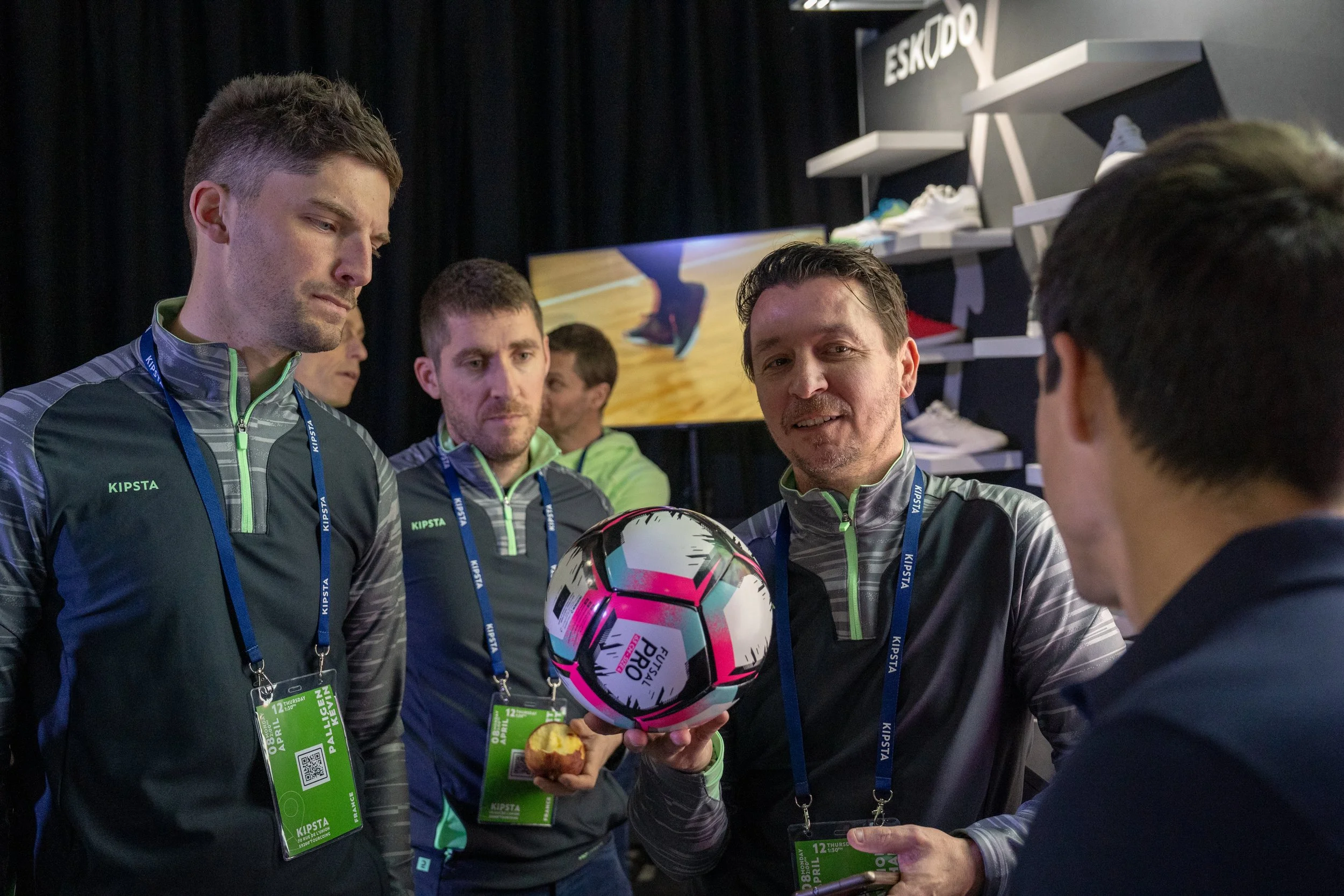 Groupe de personnes en vêtements de sport discutant lors d'un événement, avec un homme tenant un ballon de football.