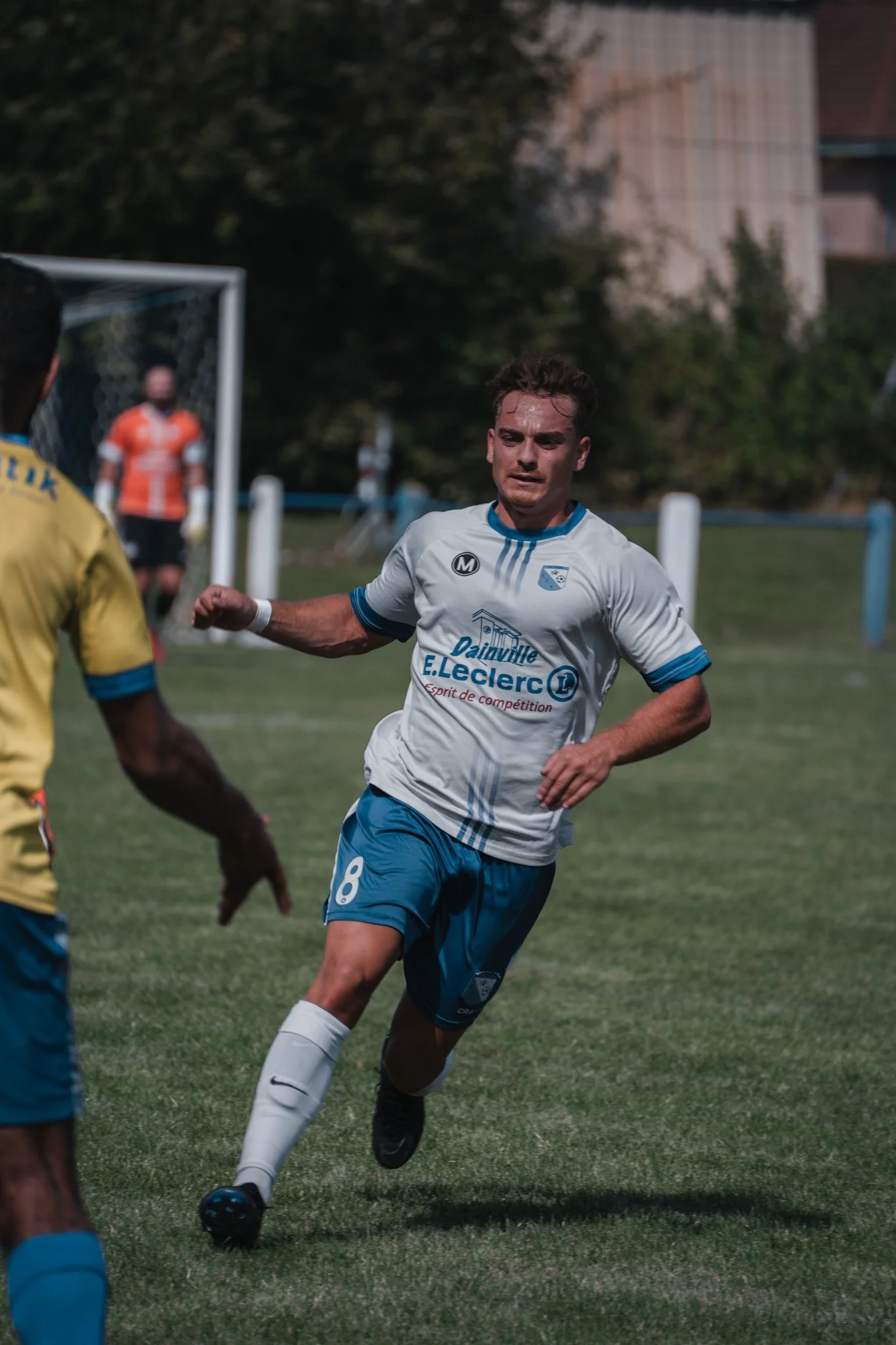 Un joueur de football en train de courir sur le terrain, portant un maillot blanc avec le logo de E.Leclerc et le numéro 8, en pleine action lors d'un match.