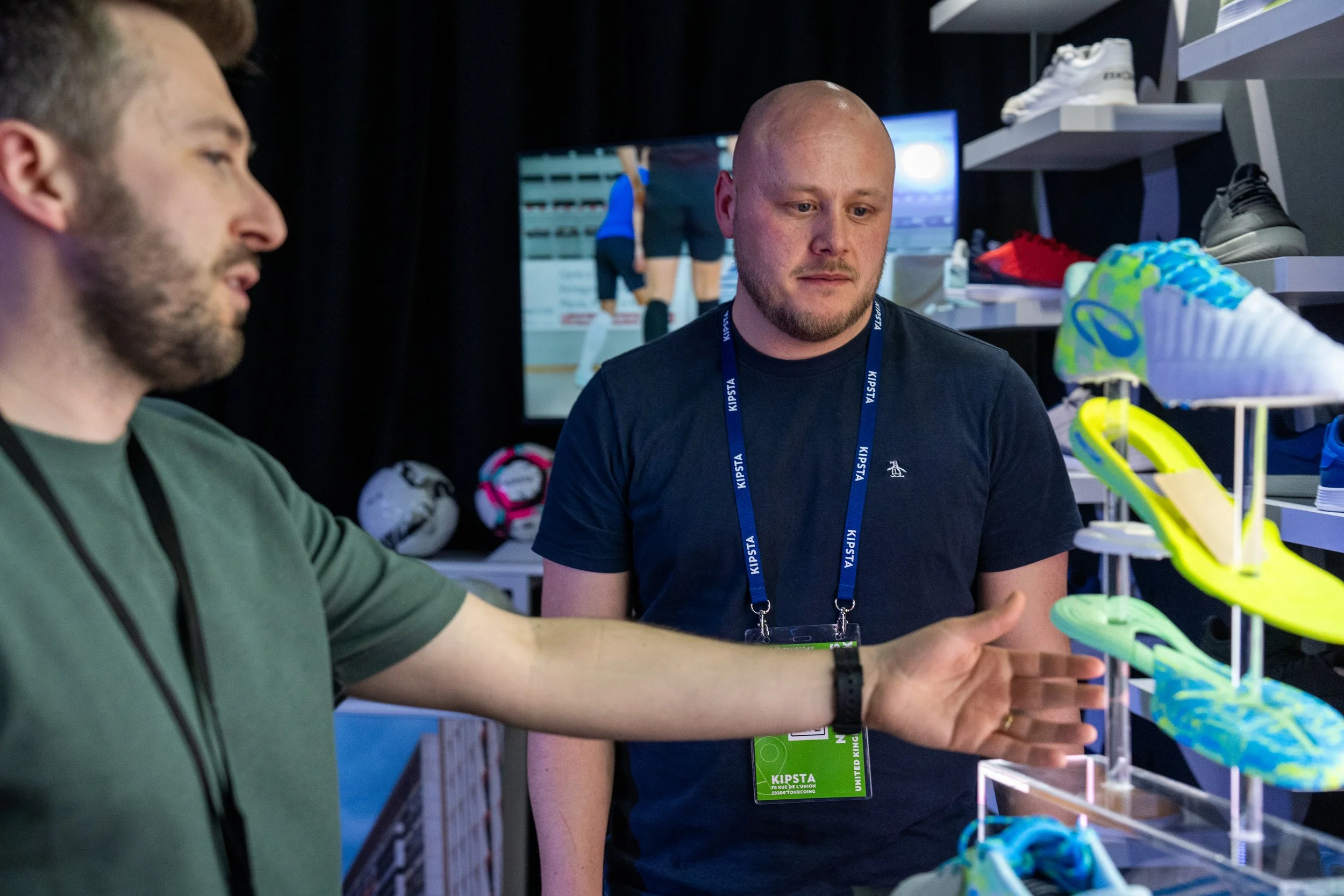 Deux hommes discutent devant un stand de chaussures de sport, avec des chaussures colorées exposées.