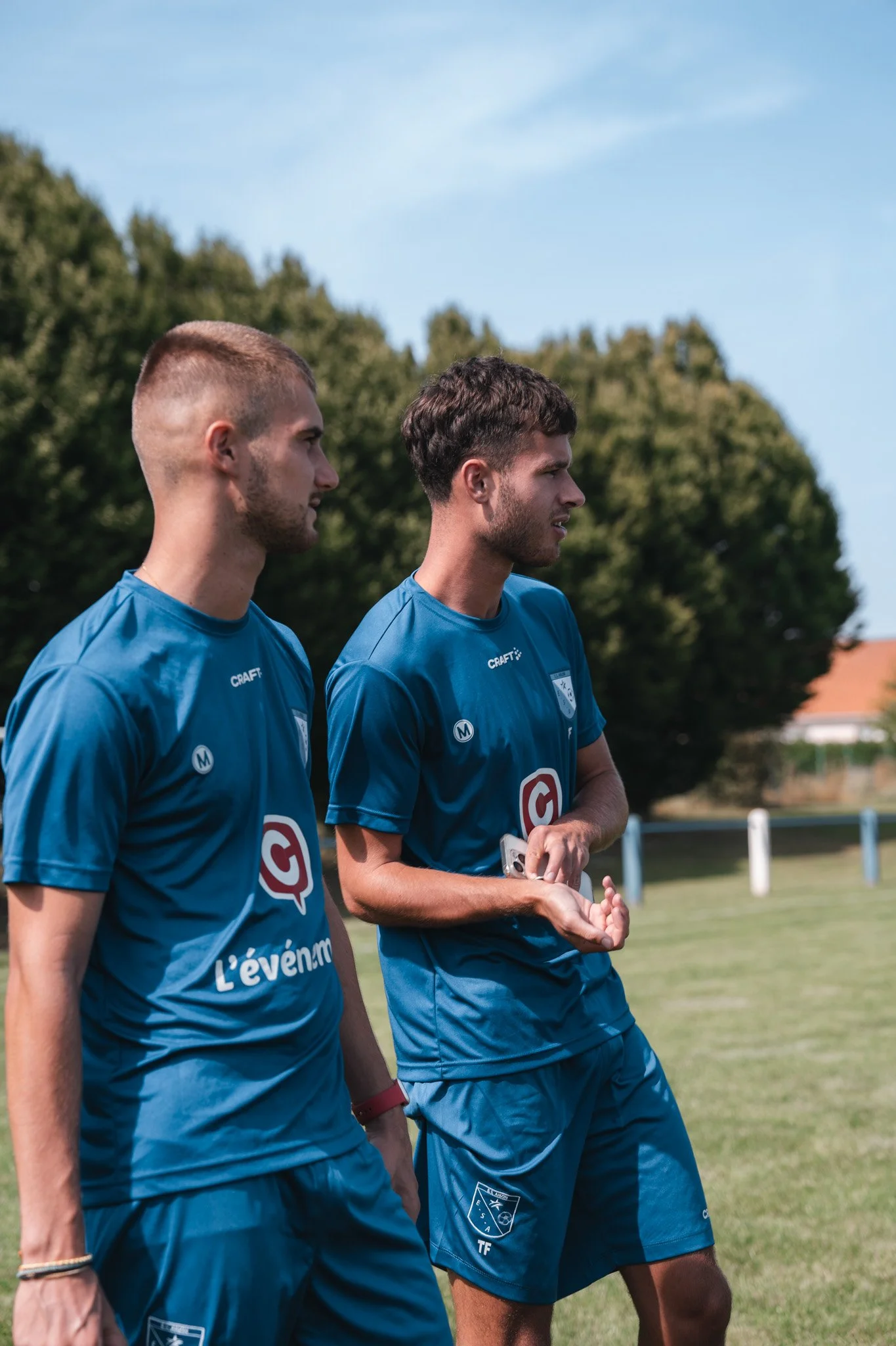 Deux joueurs de football en uniforme bleu discutent lors d'un entraînement en plein air.
