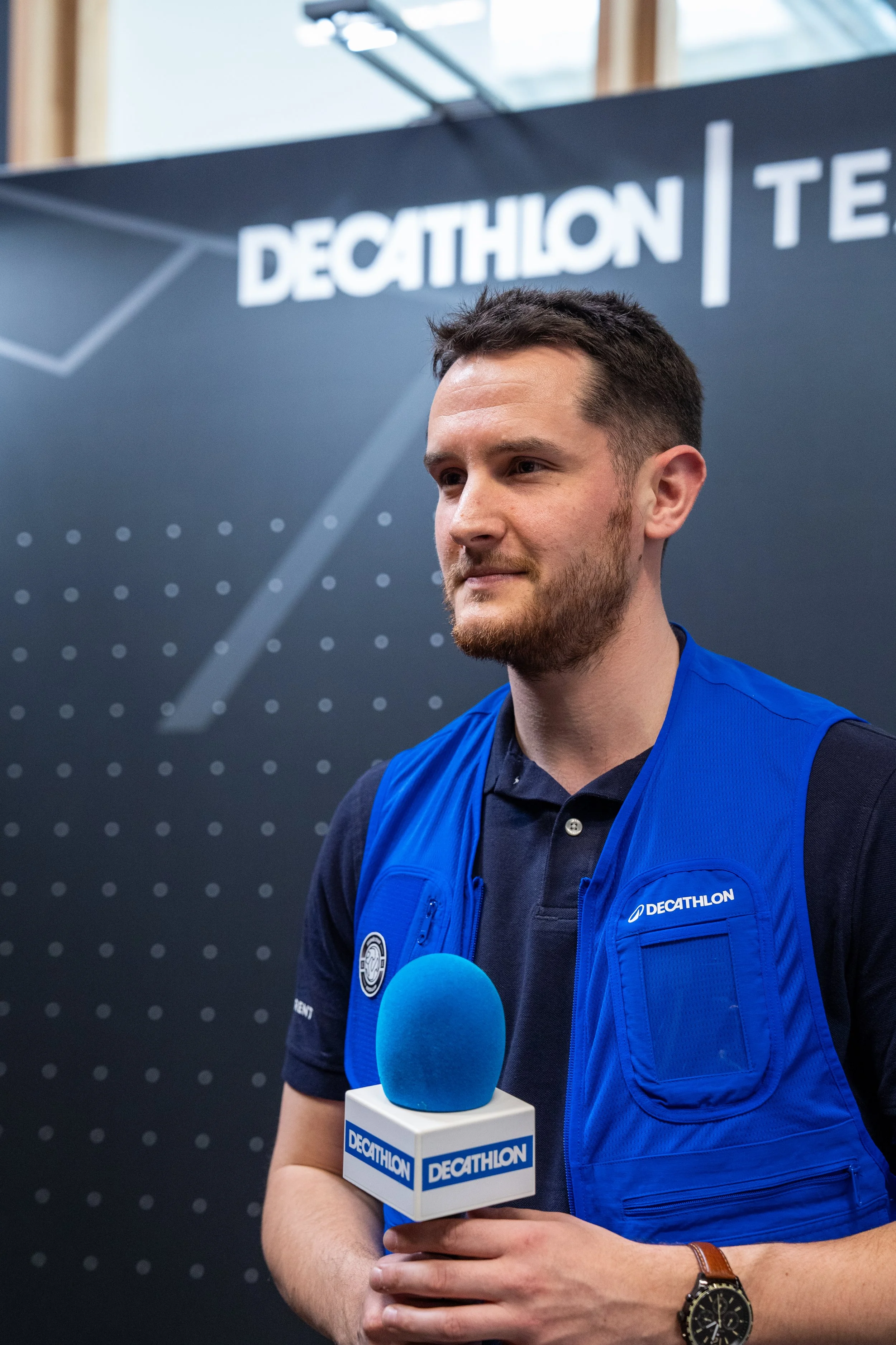 Un homme tenant un micro lors d'une interview, portant un gilet bleu avec le logo 'Decathlon'.