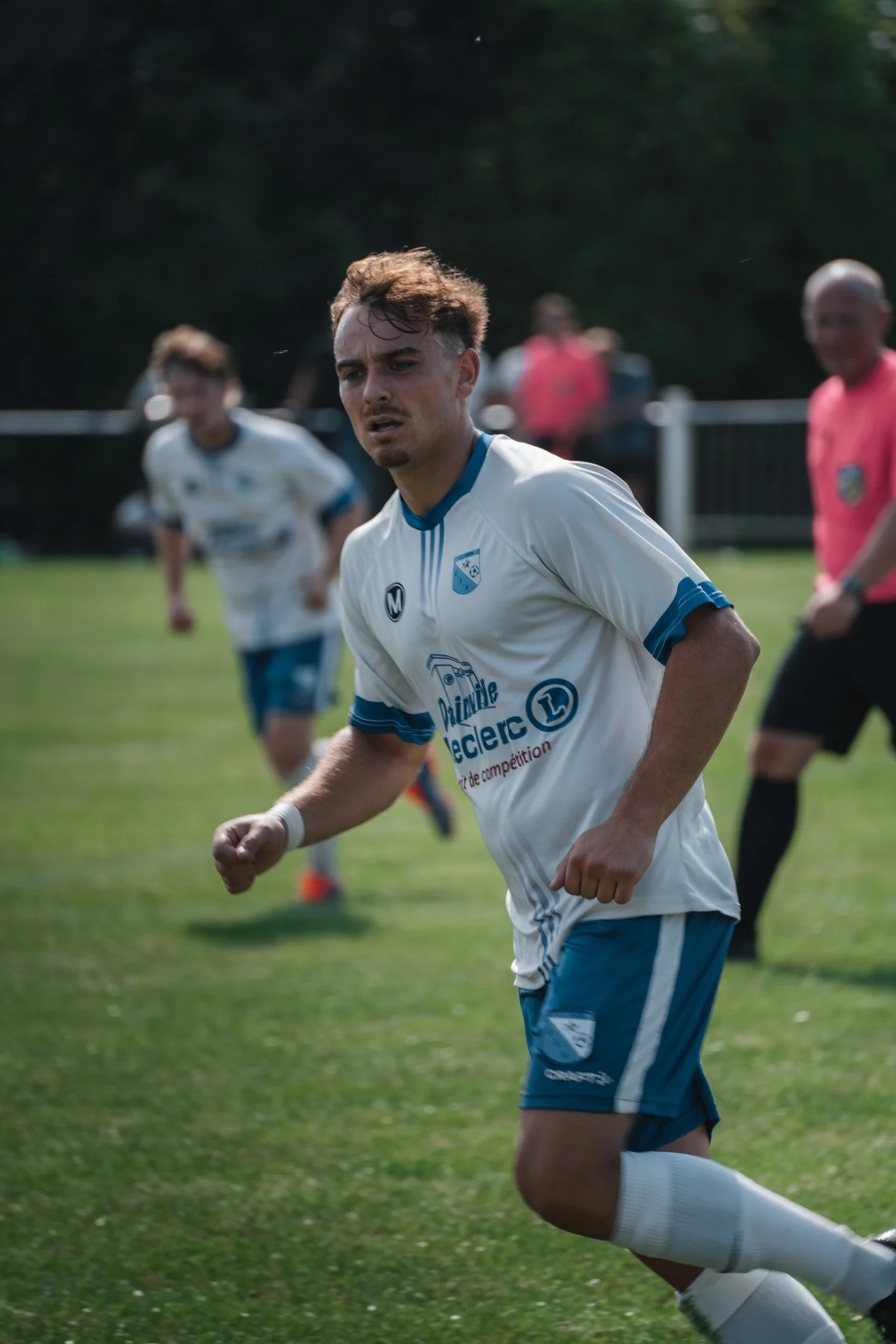 Un joueur de football en mouvement sur le terrain, portant un maillot blanc avec des détails bleus, lors d'un match.